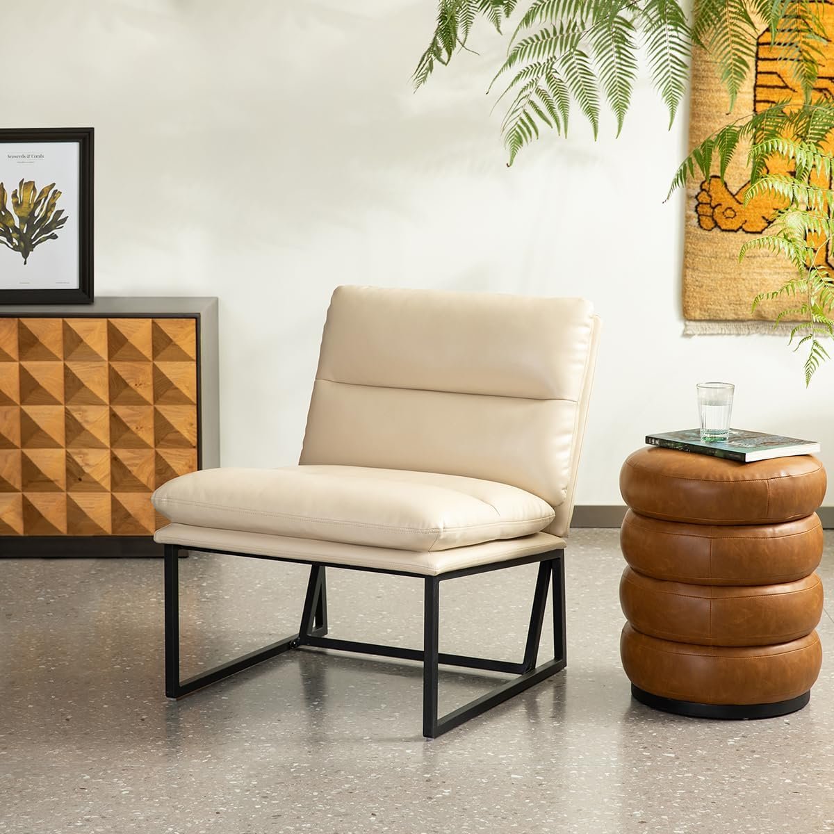 A modern armless slipper chair with a cream leather seat and a black metal sled base sits next to a stack of brown leather poufs.