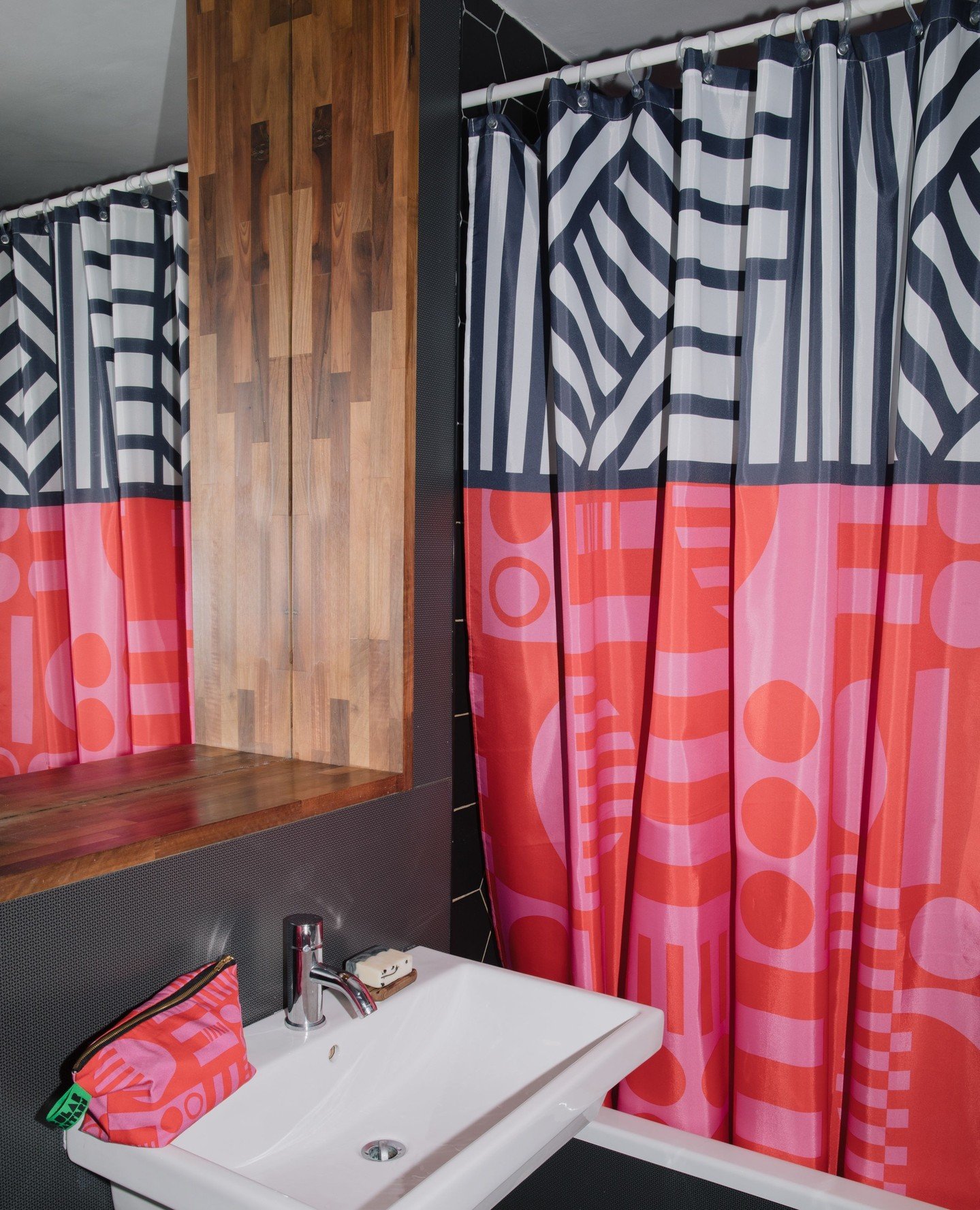 A maximalist shower curtain divided into two halves: the top has navy blue and white geometric and striped patterns, and the bottom is solid hot pink with faint orange geometric shapes.
