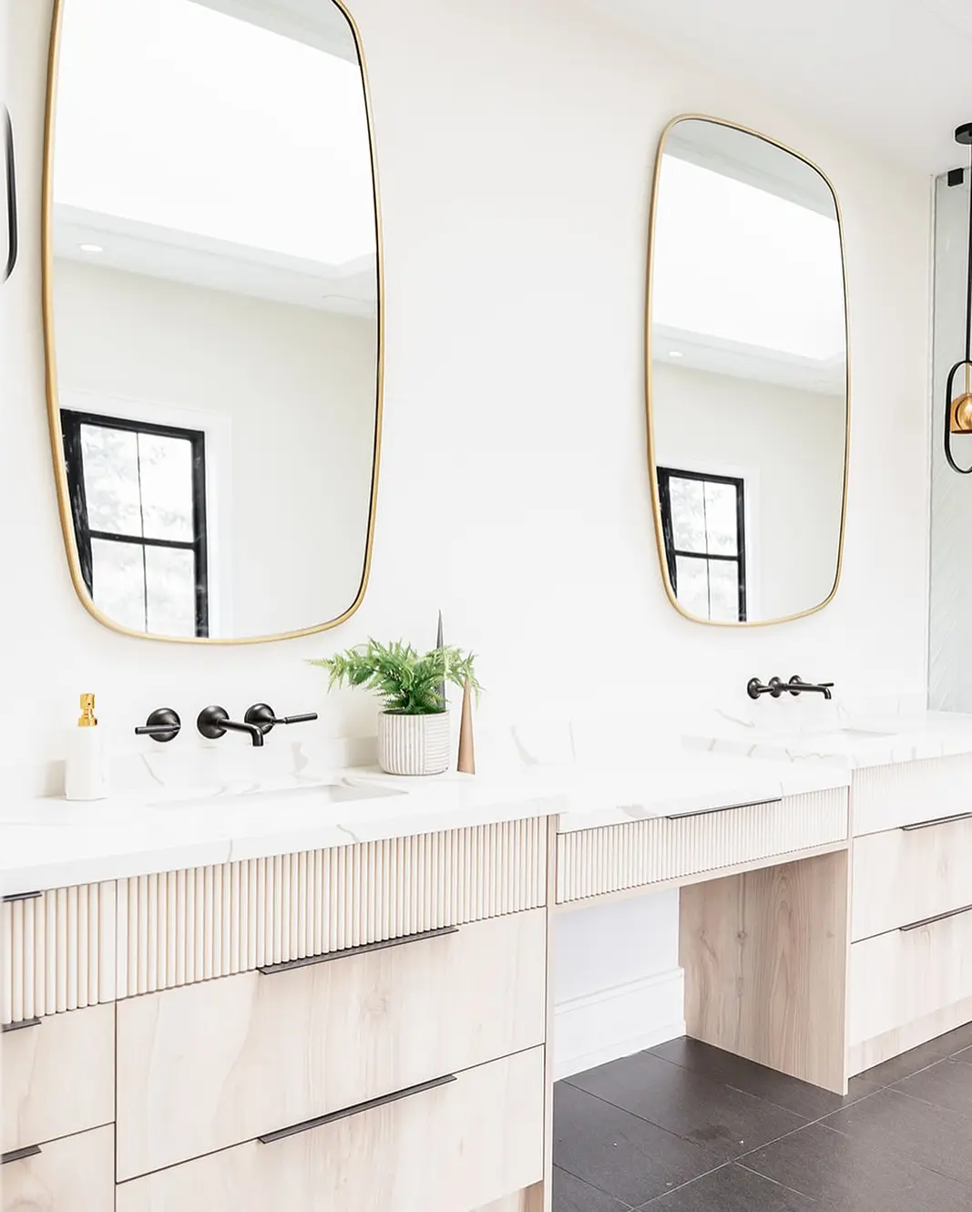 A modern bathroom with two tall, golden-framed mirrors with rounded corners above a double sink vanity.
