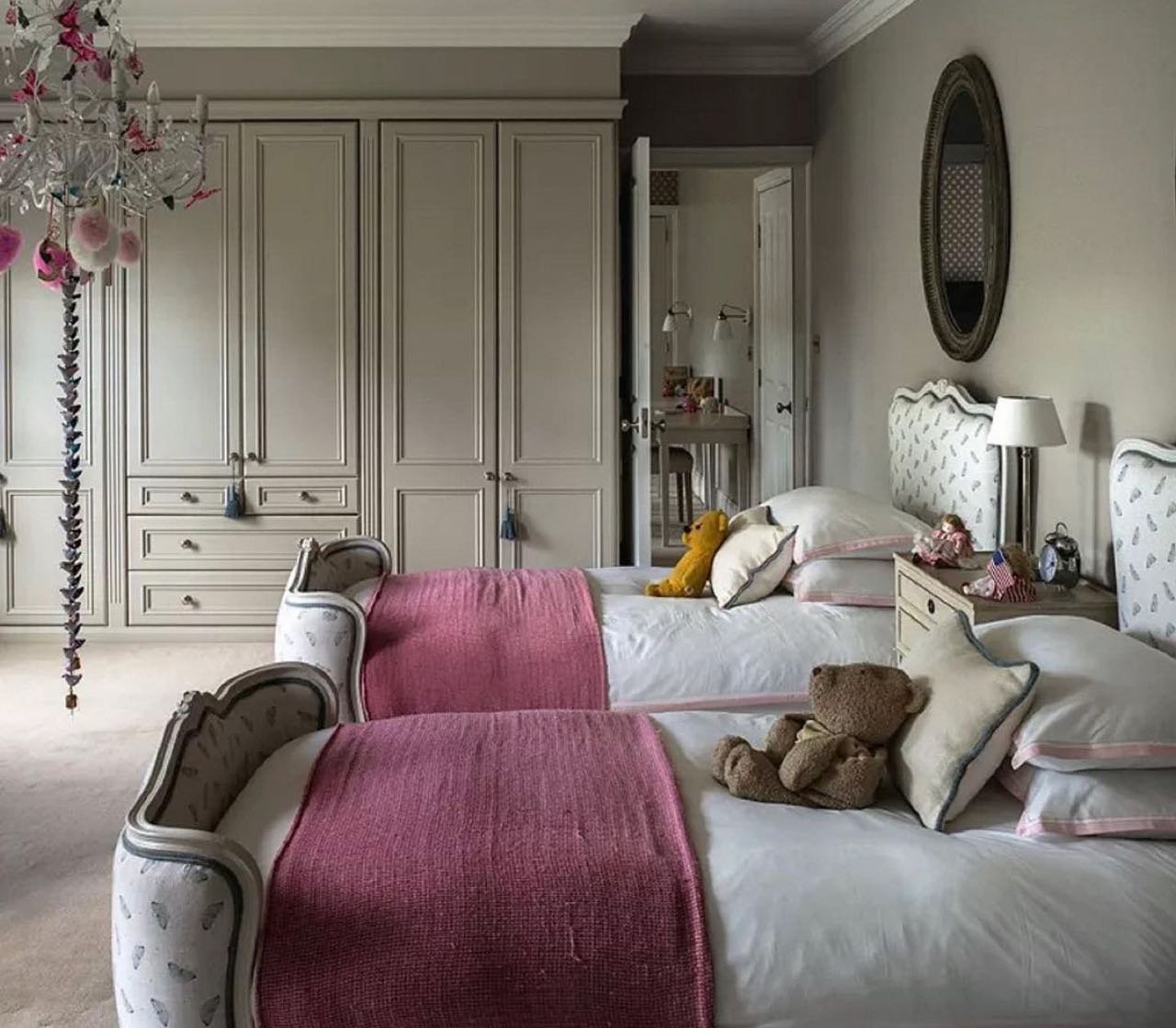 An elegant twin bedroom with two beds, upholstered headboards, pink blankets, and a whimsical chandelier.