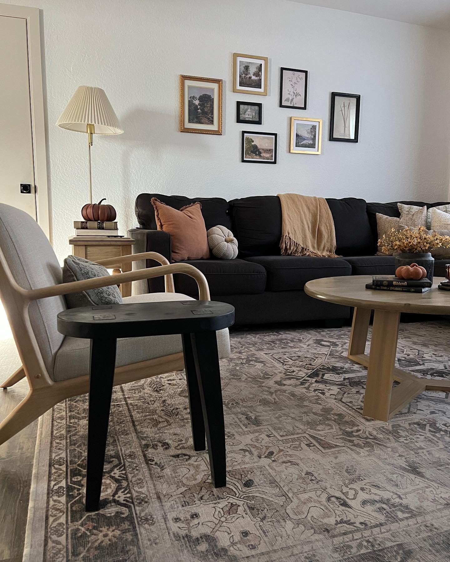 Dark living room with a black sectional sofa, a tan throw blanket, and a gallery wall with ornate gold frames.