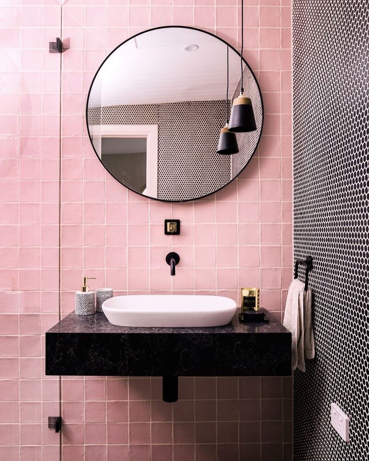 A small, modern bathroom with a pink tiled wall and a black honeycomb tiled wall.