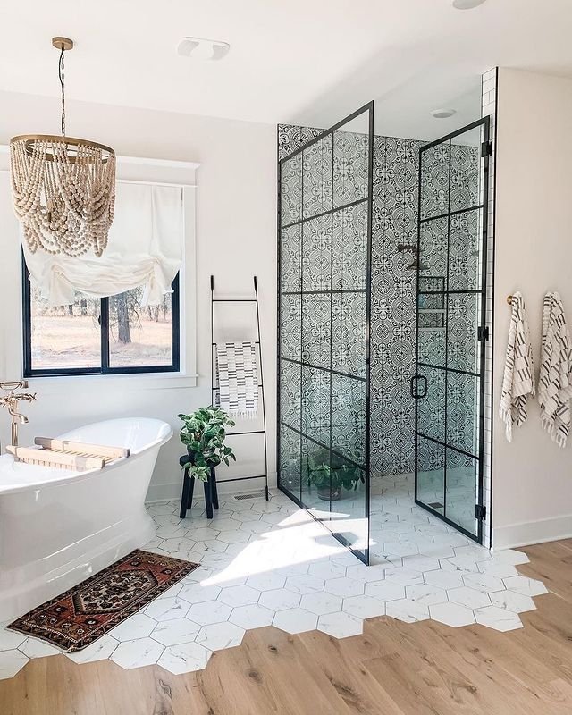 A bright farmhouse bathroom featuring a walk-in shower enclosed by black, grid-patterned metal and glass doors, revealing a back wall of black-and-white patterned tile.