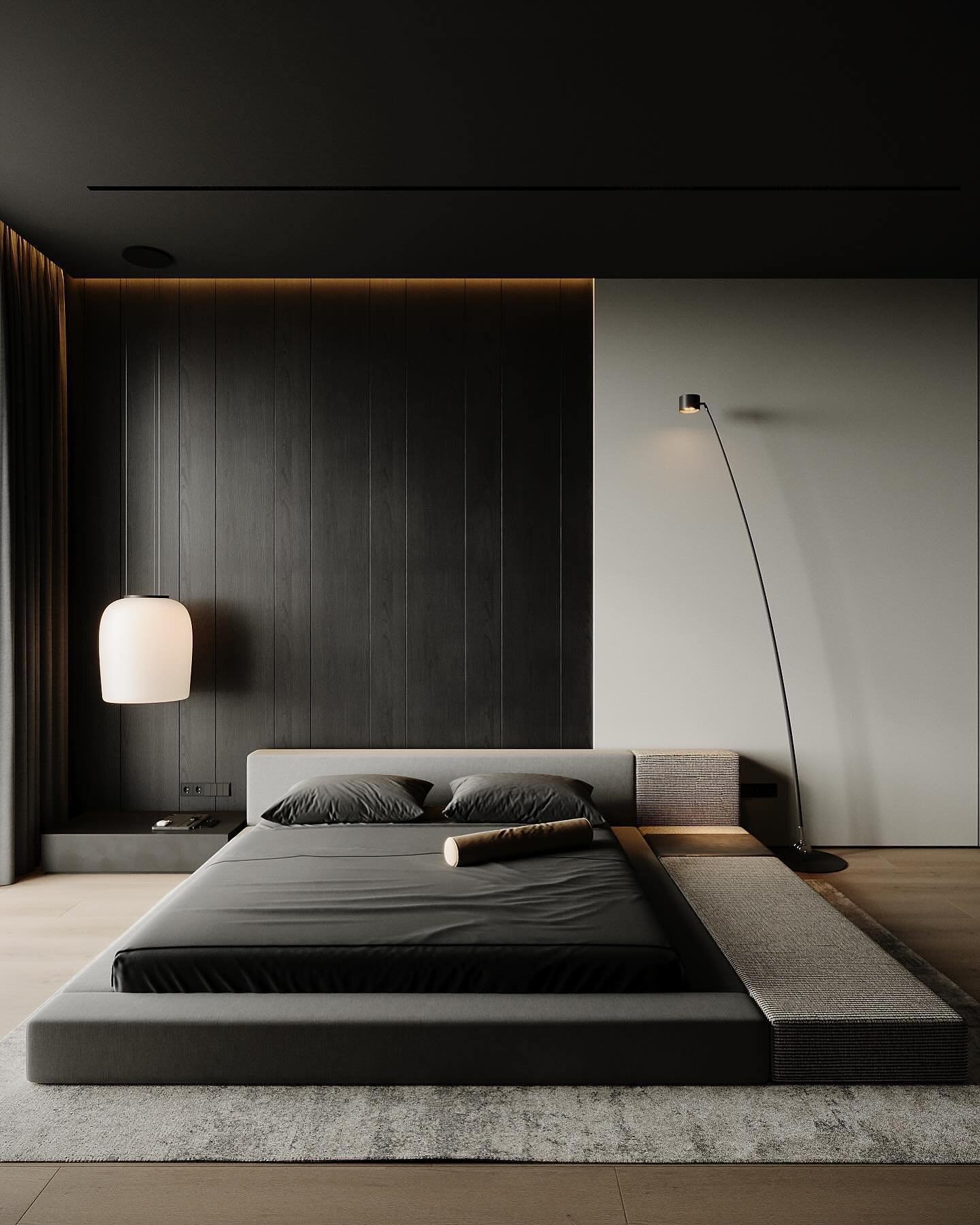 A modern bedroom with a black wood accent wall, a light grey wall, a low-profile platform bed, a sculptural floor lamp, and a white pendant light.