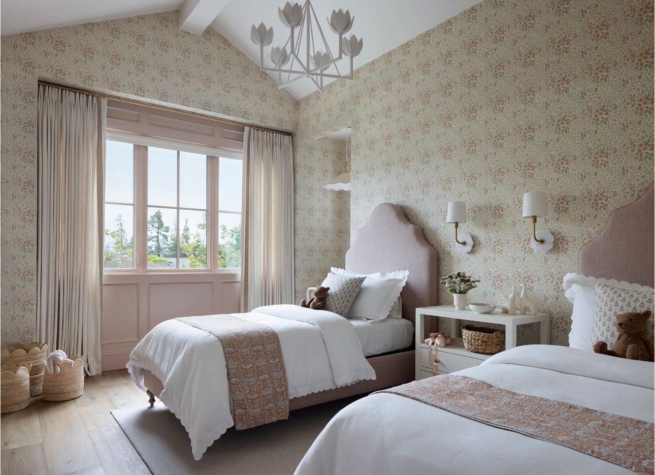 A twin bedroom with pink velvet arched headboards, floral wallpaper, and a unique chandelier.
