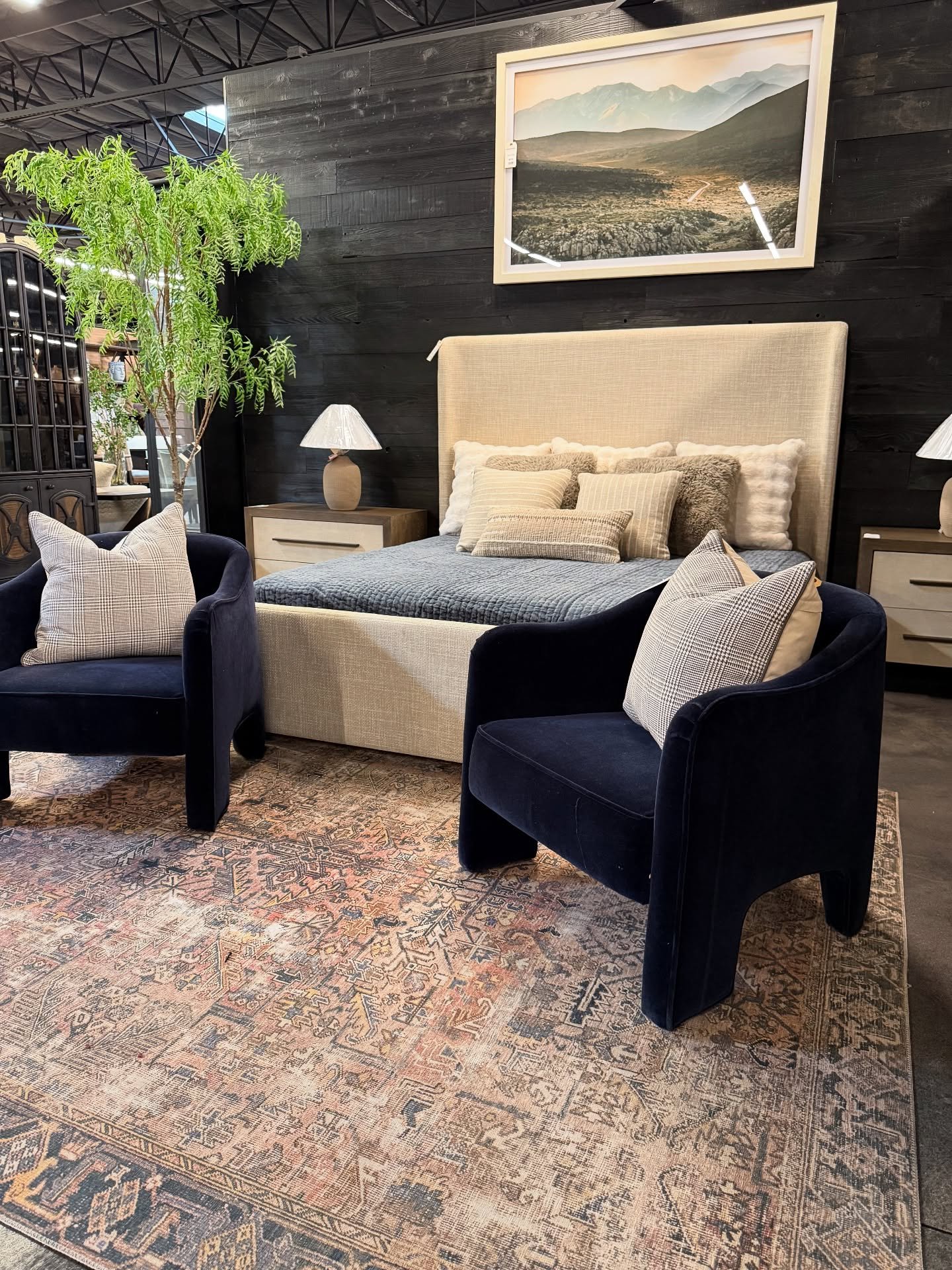 A pair of large, dark navy blue velvet armchairs with modern, sculptural shapes sit on a patterned rug at the end of a bed.
