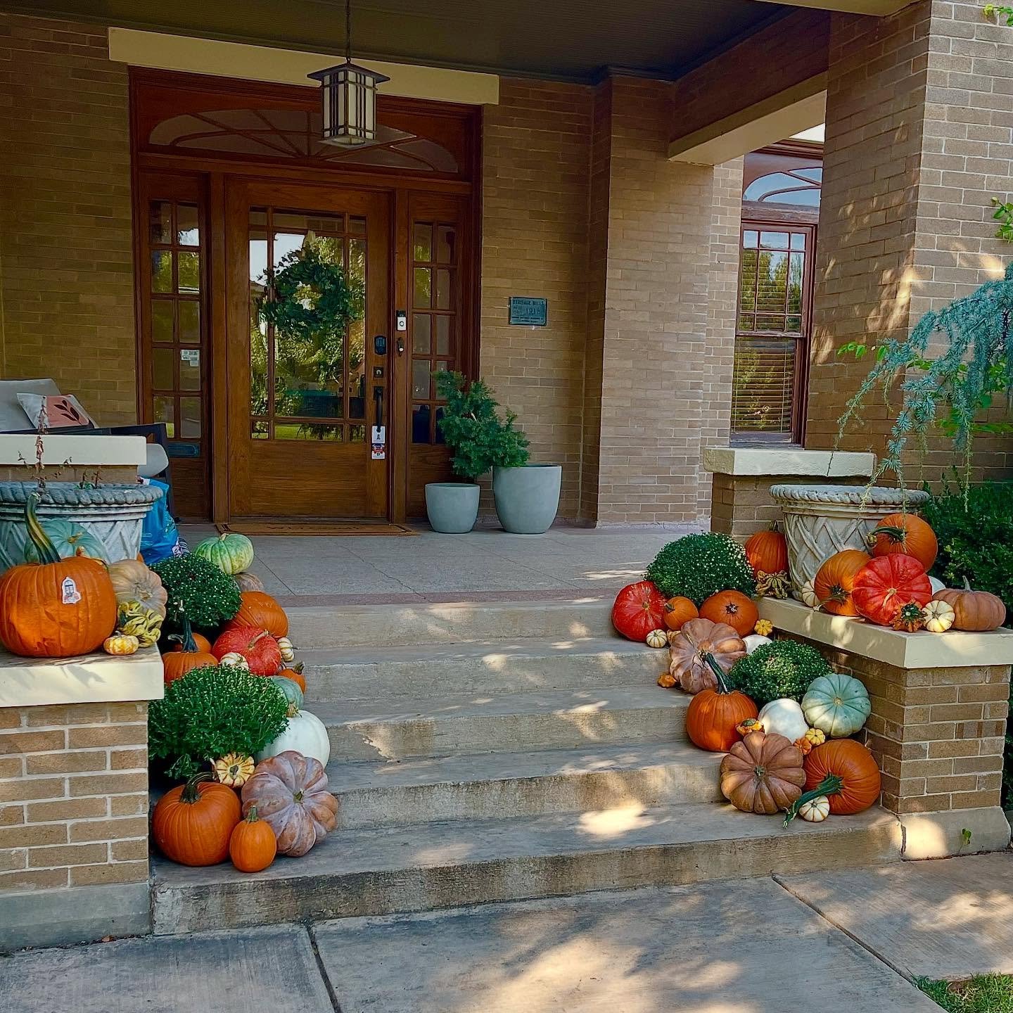 A brick porch with a staircase completely covered with a mix of pumpkins and gourds in various sizes and colors, creating a beautiful fall display.