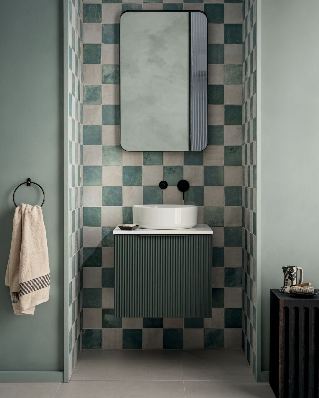 A small bathroom sink area featuring a white vessel sink on a dark green ribbed floating cabinet.