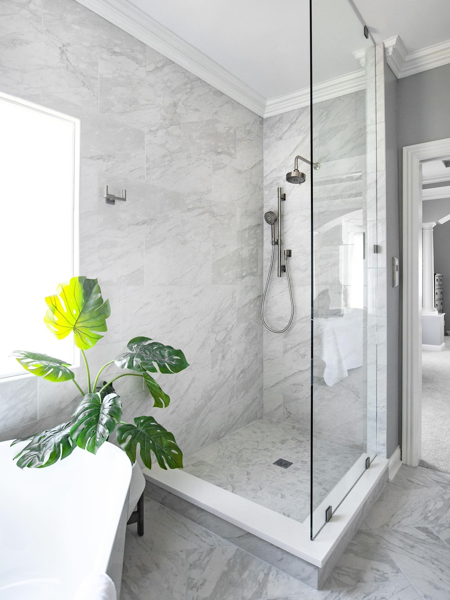 A luxurious, bright walk-in shower entirely clad in large-format light gray and white marble-look tiles with polished chrome fixtures and frameless glass.