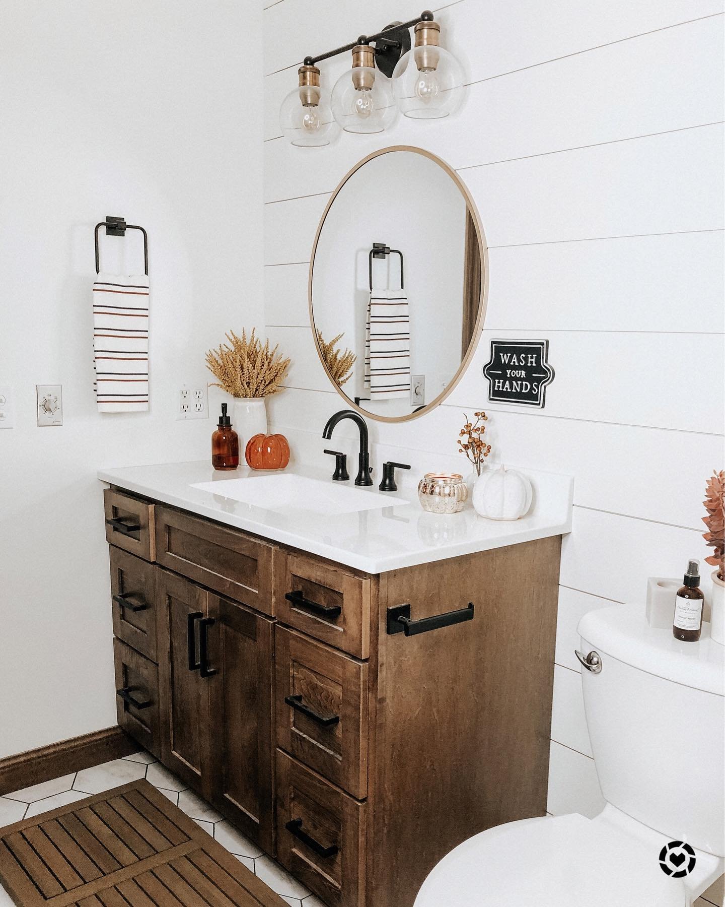 A modern bathroom with white shiplap walls, a wooden vanity, and a vase of dried wheat stalks on the counter.