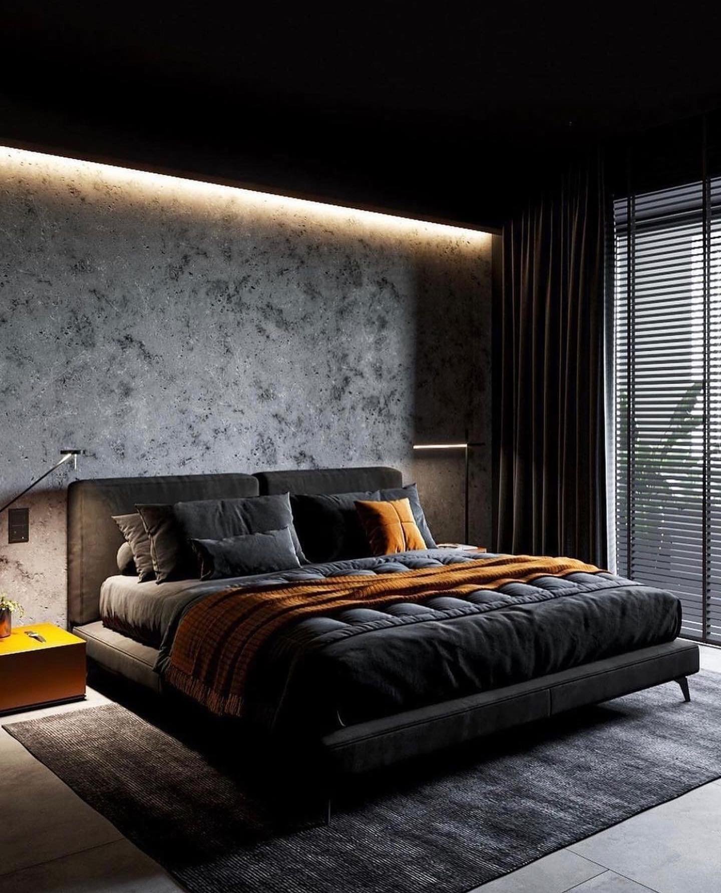 A dark bedroom with a textured grey concrete wall, a black bed, and a vibrant orange blanket.