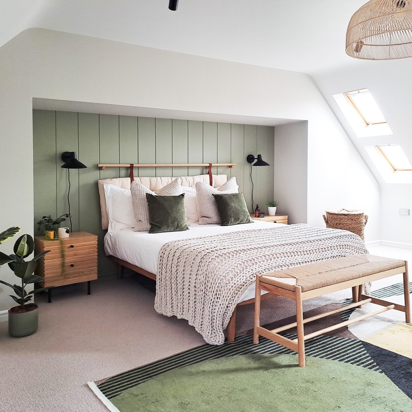 A bright loft bedroom with a bed in a recessed nook with a green slatted accent wall, a chunky knit blanket, and light wood furniture.