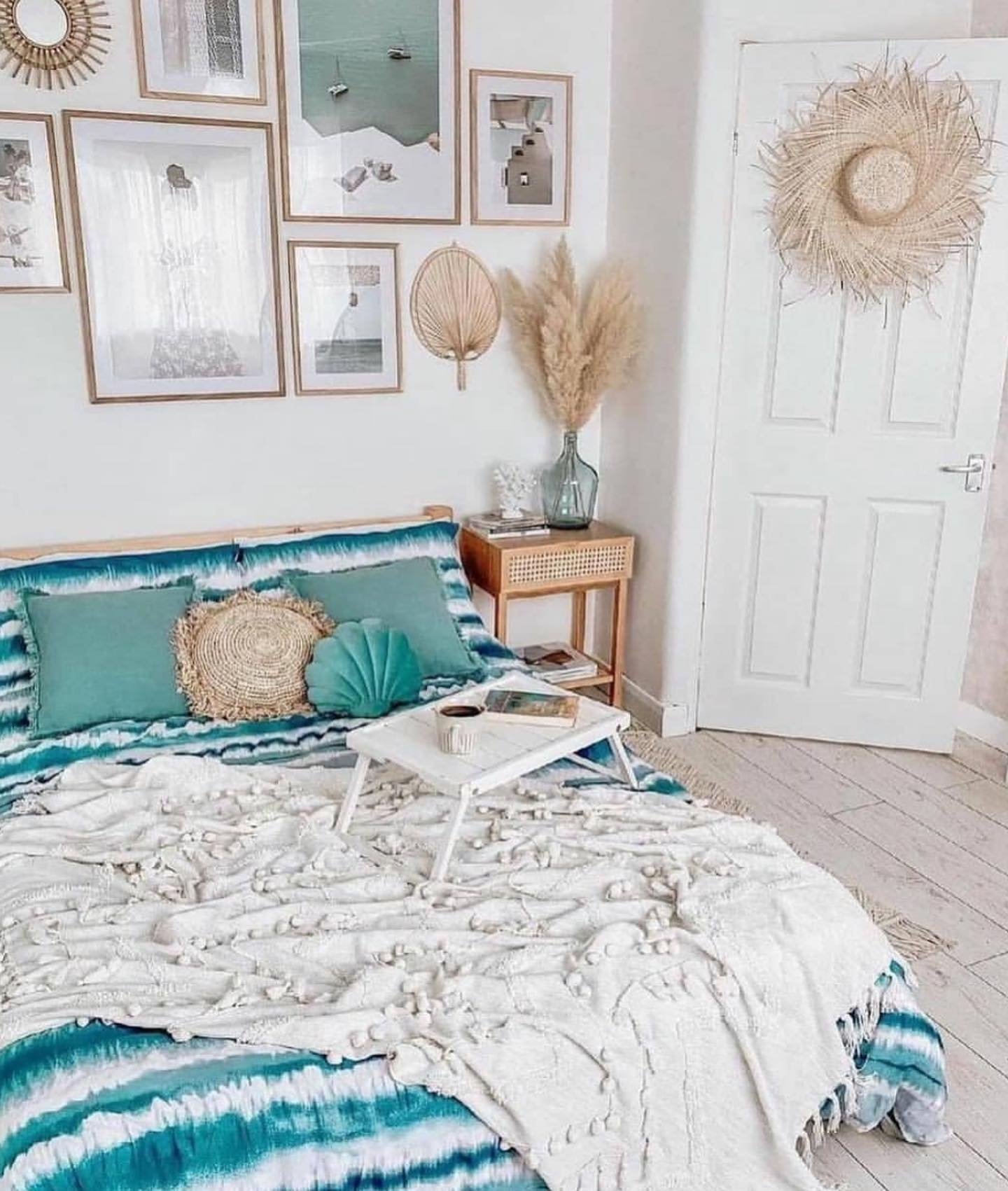 A bright boho bedroom with a coastal feel, featuring a blue and white tie-dye comforter, a gallery wall of framed art, and natural textures.