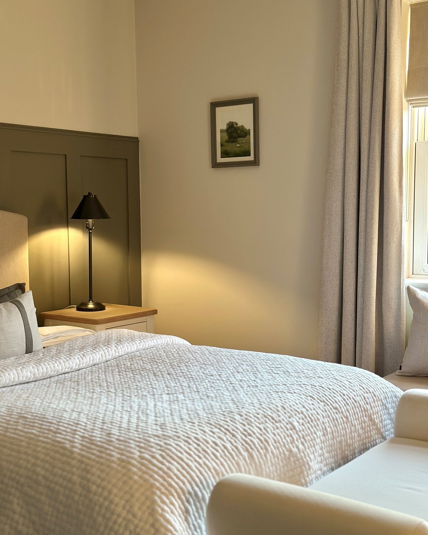 A traditional table lamp with a dark metal base and a black, bell-shaped shade sits on a light wooden nightstand.