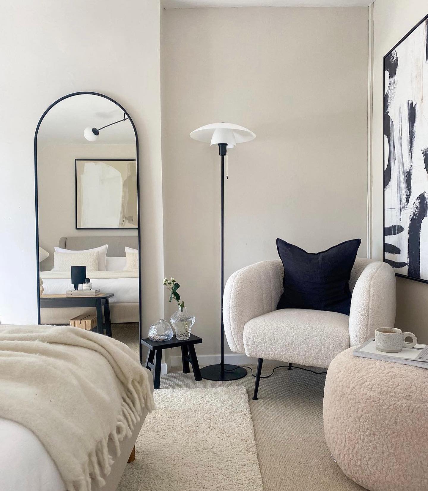 A cozy, off-white teddy-like armchair with a navy pillow sits next to a matching pouf and a floor lamp.