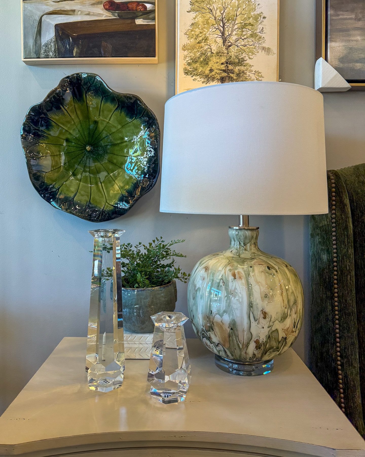 A unique, artistic table lamp with a green and white swirled ceramic base sits on a white nightstand.