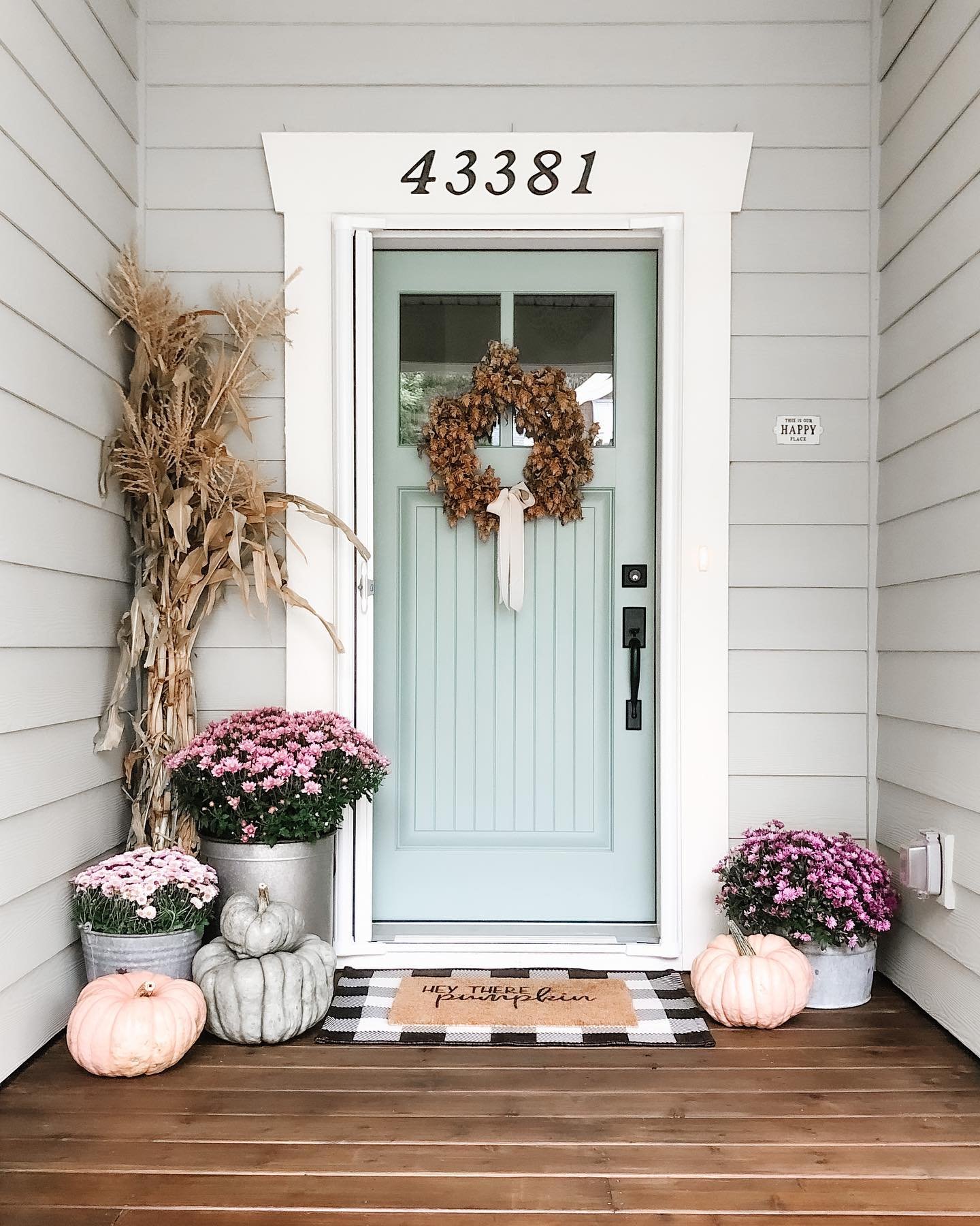 A charming fall porch decorated with bundles of cornstalks, pink and gray pumpkins, and pink mums in tin buckets.