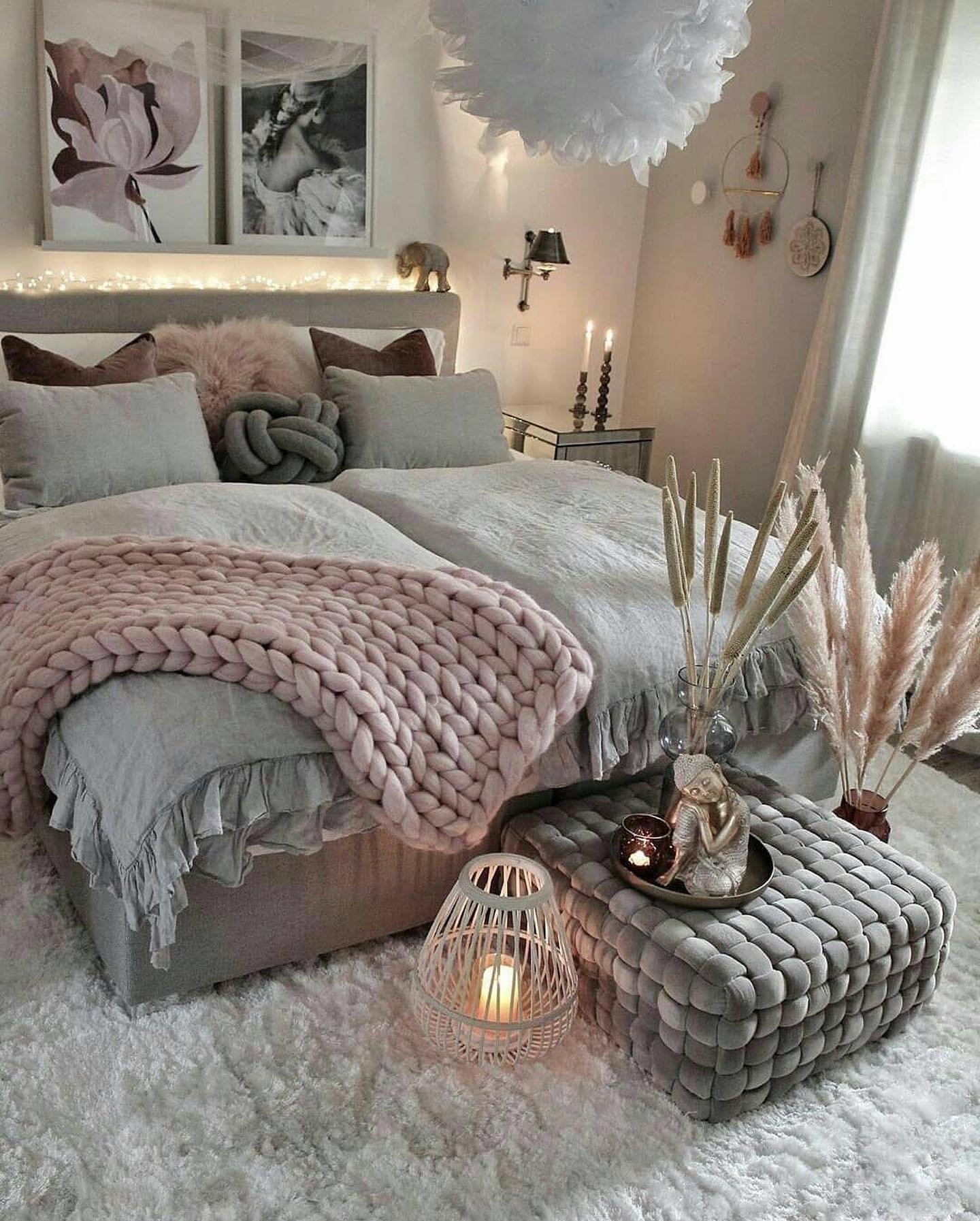A dreamy bedroom with a bed covered in gray and pink bedding, a chunky knit pink blanket, a fluffy white rug, and pampas grass in a vase.