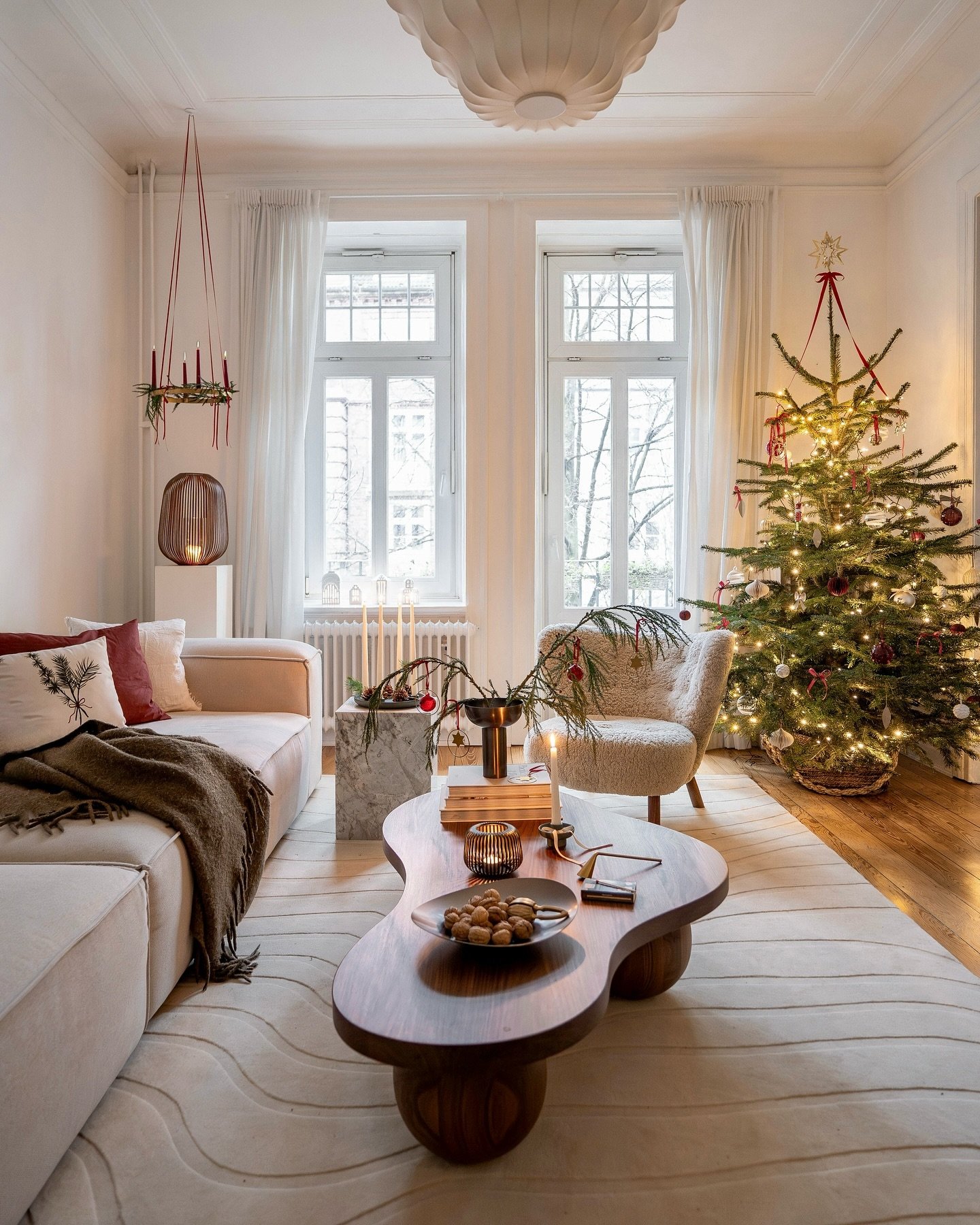 Contemporary living room with a unique wooden coffee table, blush sofa, and a natural Christmas tree decorated with red accents.