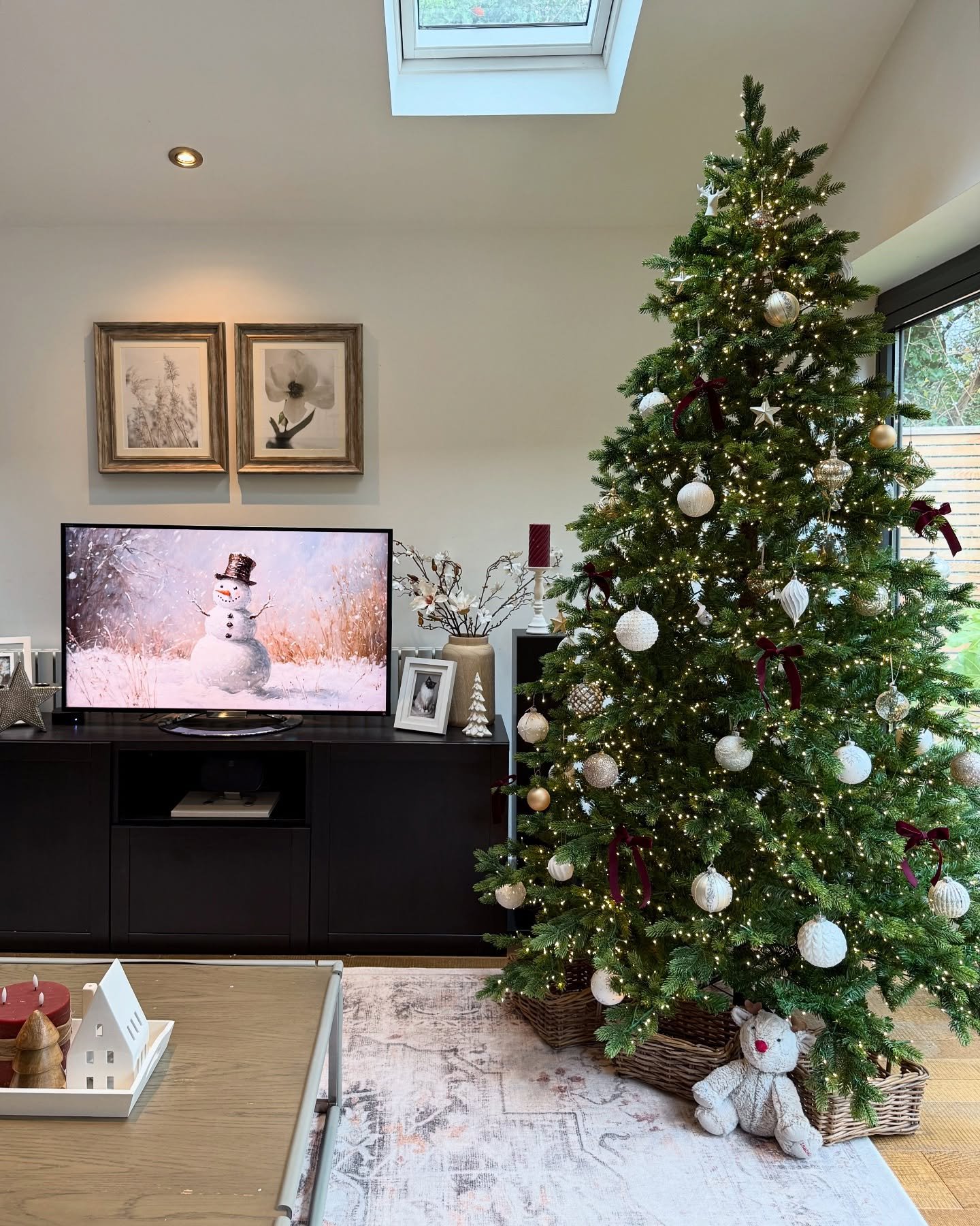 A Christmas tree decorated with a simple, cozy mix of white baubles and small burgundy velvet bows, set in a modern living room.