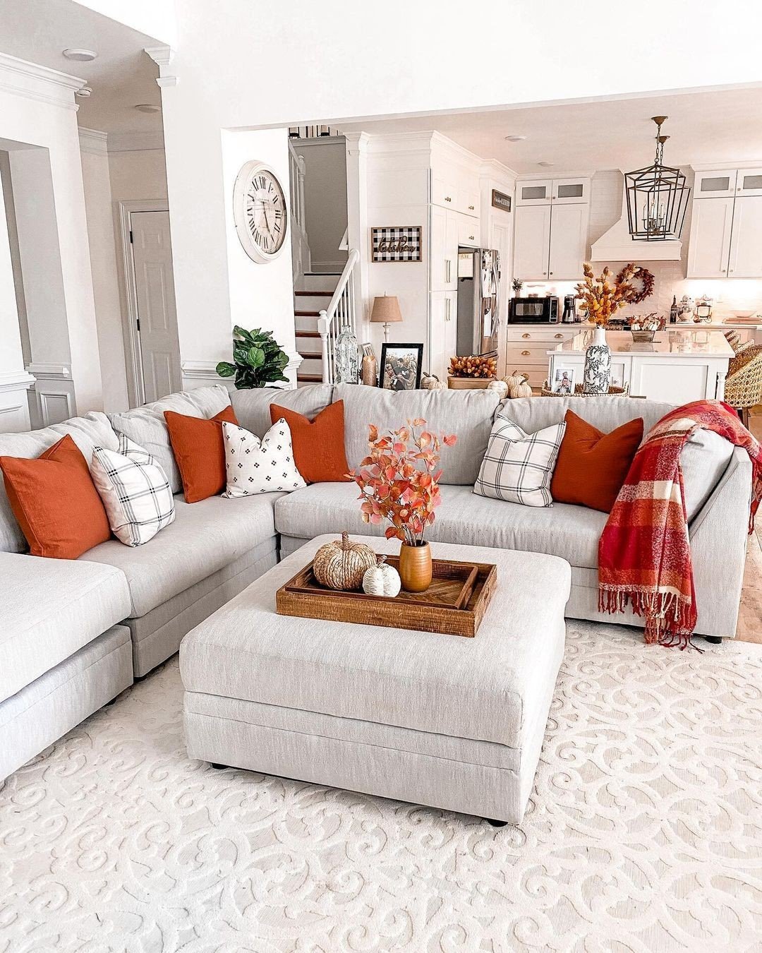 Open-concept living room and kitchen with a large sectional sofa decorated with orange and plaid pillows.