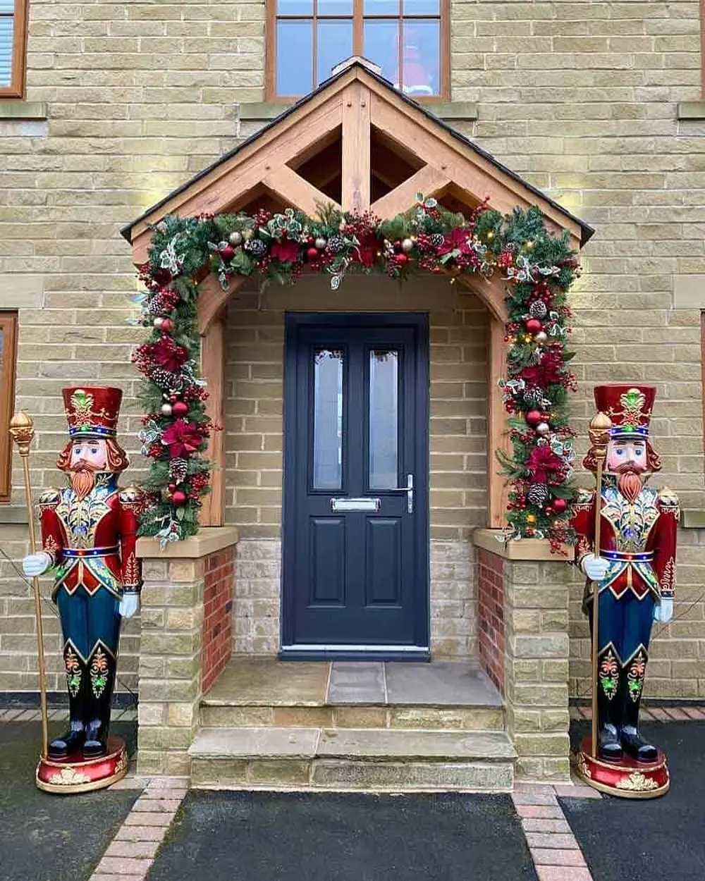 A symmetrical Christmas porch featuring two life-sized, brightly painted Nutcracker statues flanking a dark blue door, with a rich, heavily embellished garland arch.