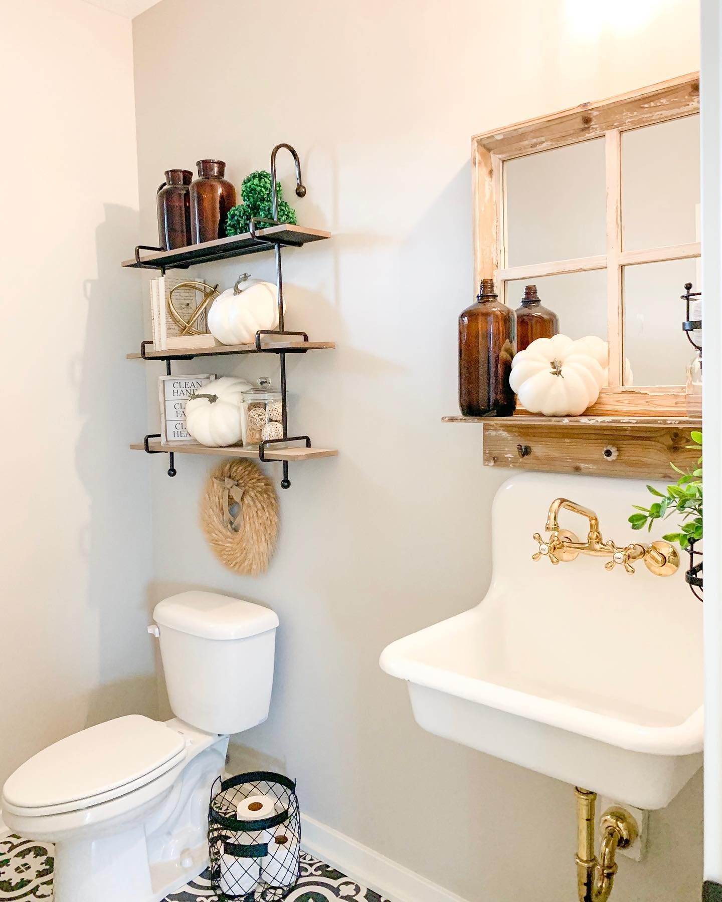 A small bathroom with a white sink and rustic mirror, decorated with white pumpkins and amber glass bottles on floating shelves.