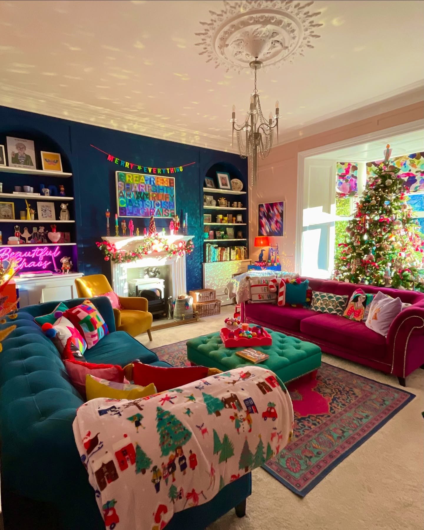 Maximalist living room featuring bright teal and magenta sofas, a colorful Christmas tree, and a neon sign with festive banners.