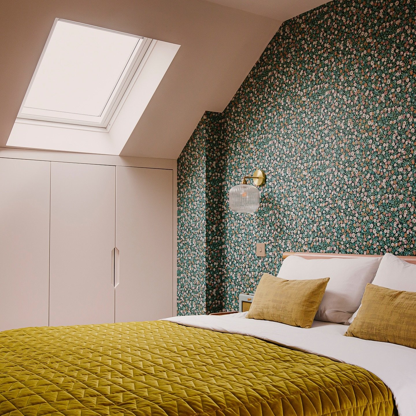 A colorful loft bedroom with a bold green floral wallpaper accent wall and a golden-yellow comforter.