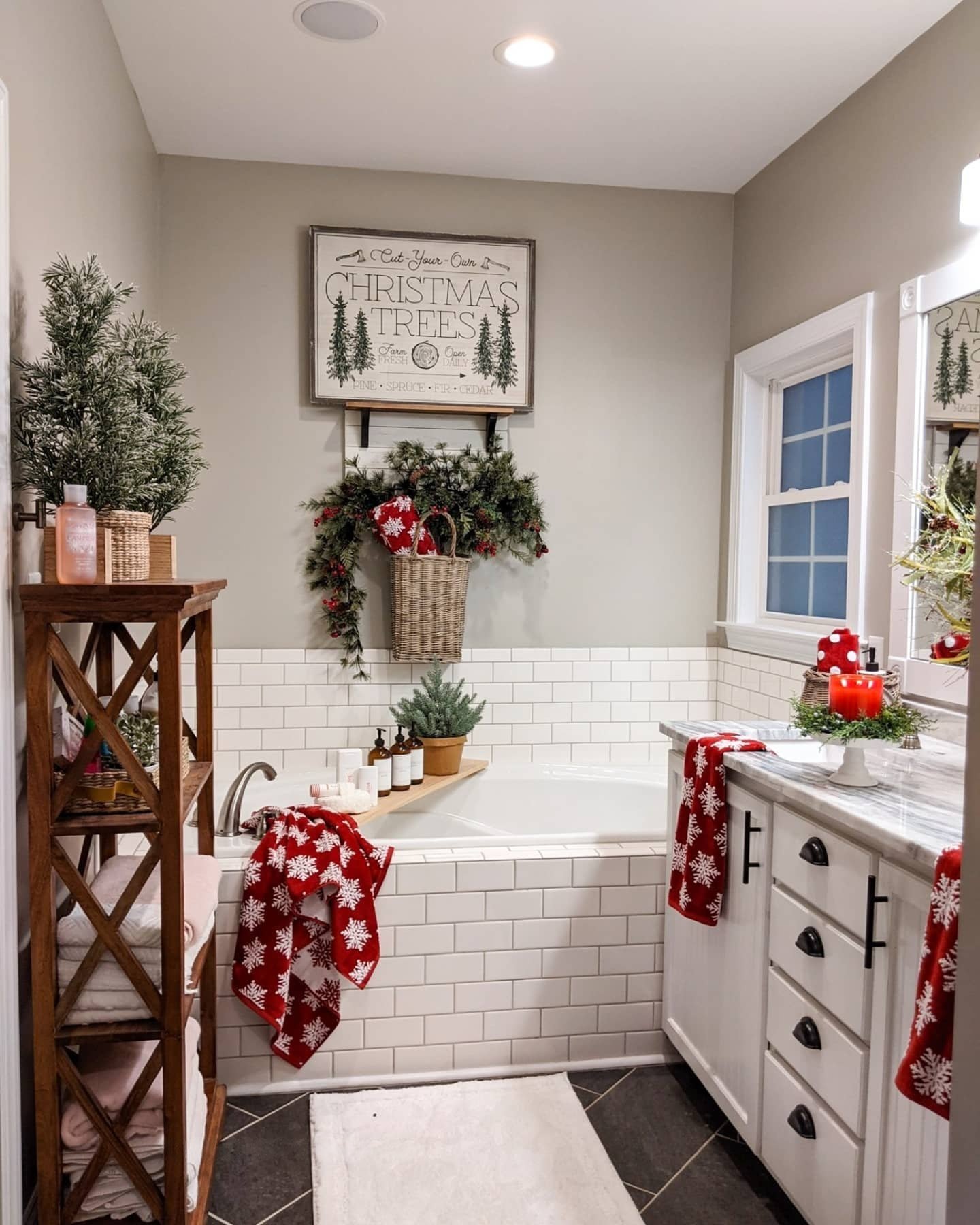 A neutral grey bathroom with white subway tile, featuring red snowflake towels, a Christmas tree farm sign, and red candles on the vanity.