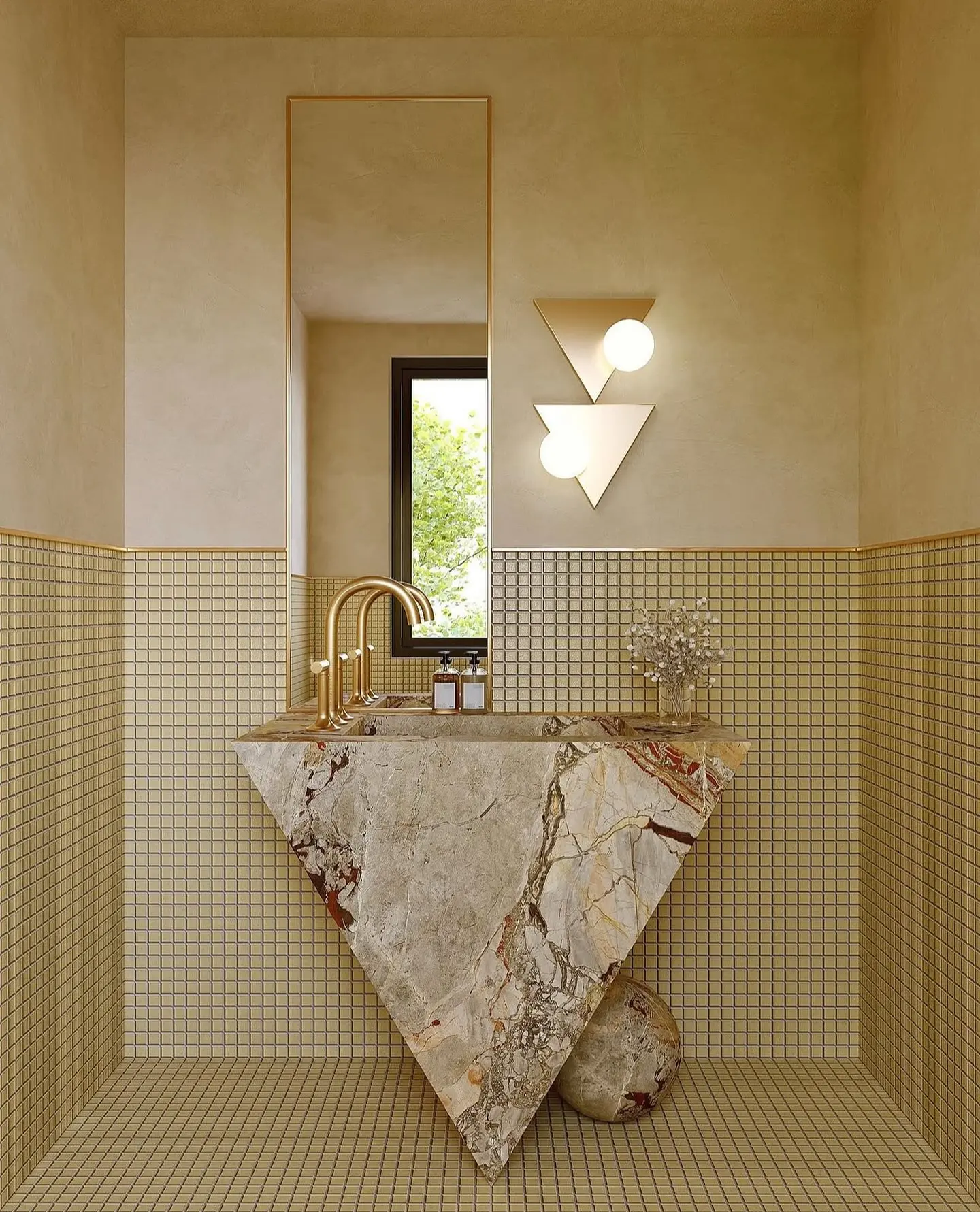 A unique bathroom with a tall, thin rectangular mirror with a gold frame above a sculptural marble sink.