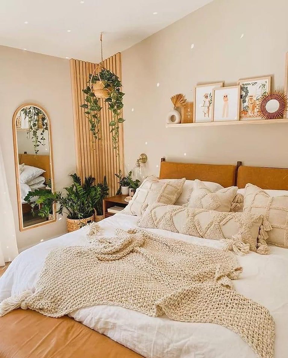 A cozy boho bedroom with a camel-colored leather headboard, a chunky knit throw, and a corner of plants and a wood slat wall.