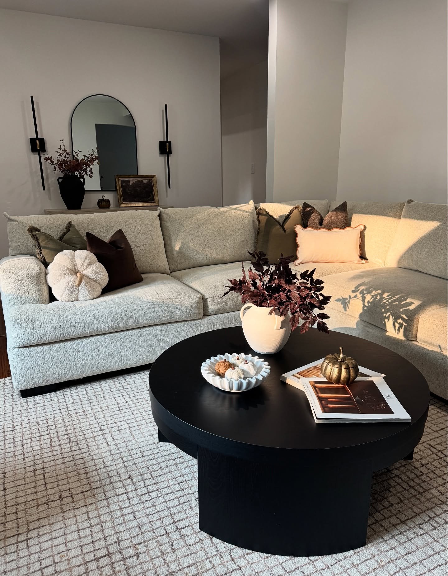 Modern living room with a light-colored sectional sofa, a black coffee table, and a vase with dark red flowers.