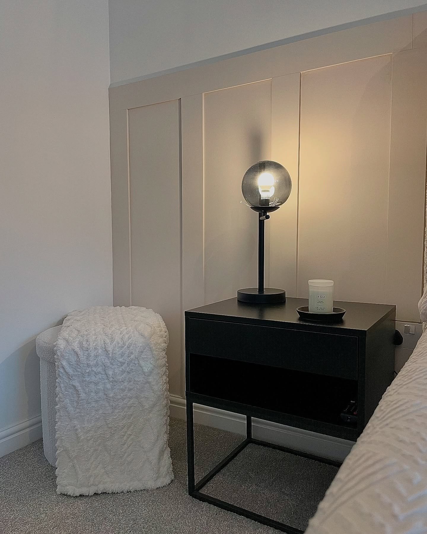 A modern, black metal table lamp with a dark, smoked glass globe shade sits on a black nightstand.