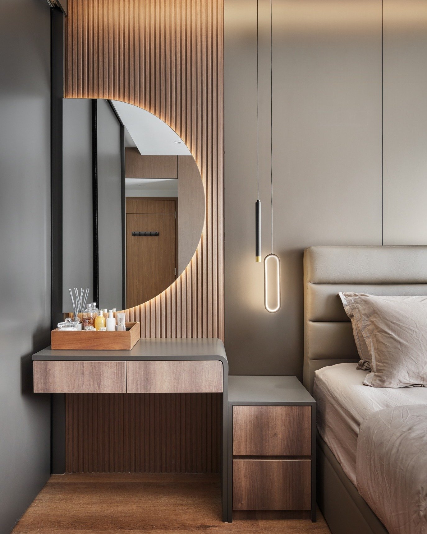 A modern bedroom vanity with a large, semicircular mirror that has built-in lighting and a floating wood desk.