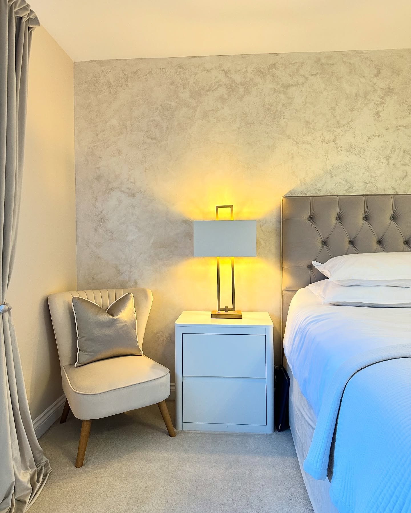 A sleek, modern table lamp with a rectangular white shade and a gold, cage-like metal base on a white nightstand.