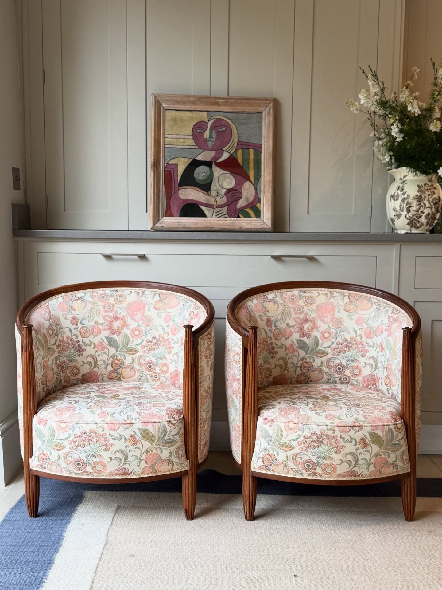 A pair of vintage-style barrel chairs with floral upholstery and dark wooden frames sit side by side on a rug.