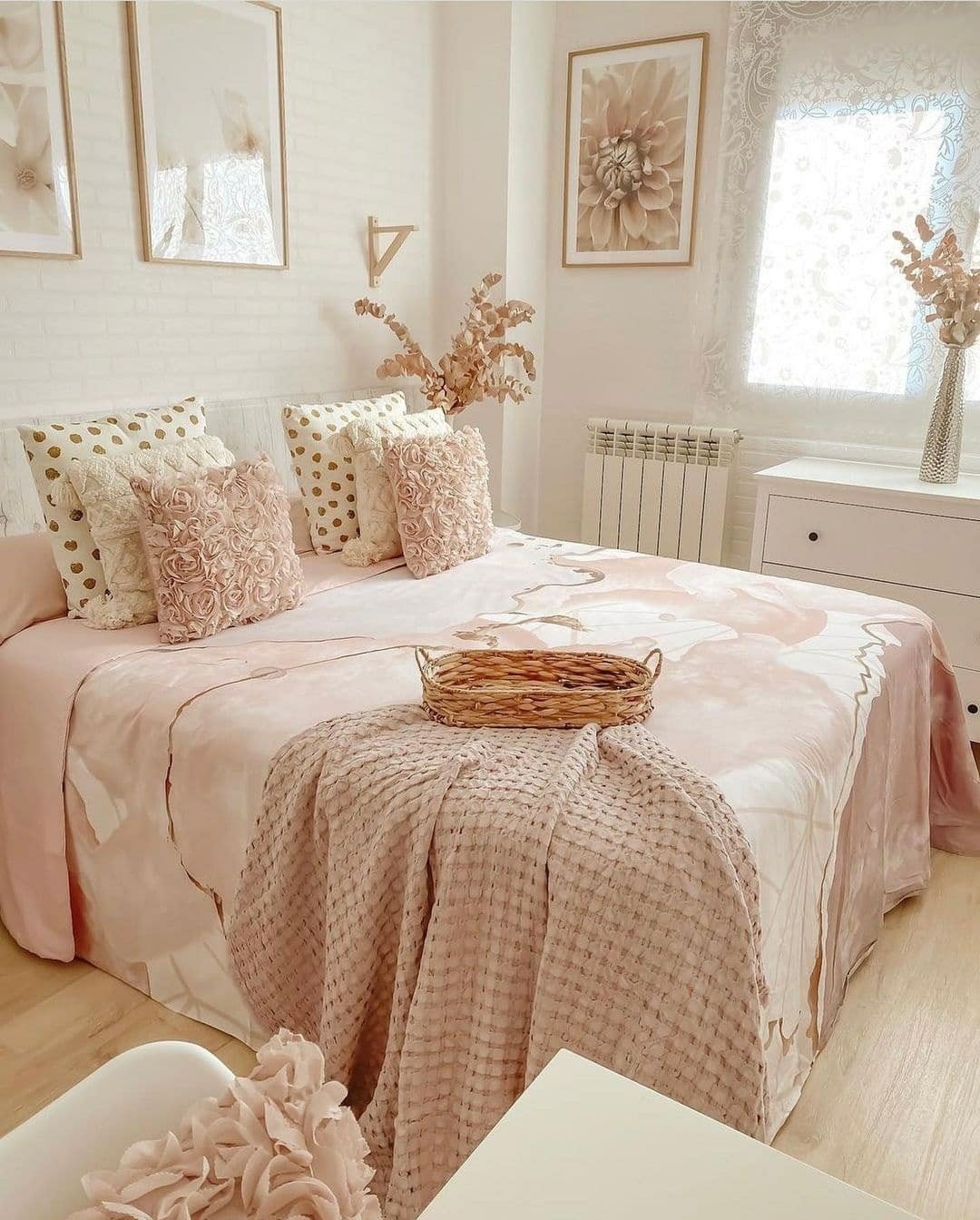 A soft, feminine boho bedroom with a pink and white color scheme, floral art, and a mix of textures on the bed.