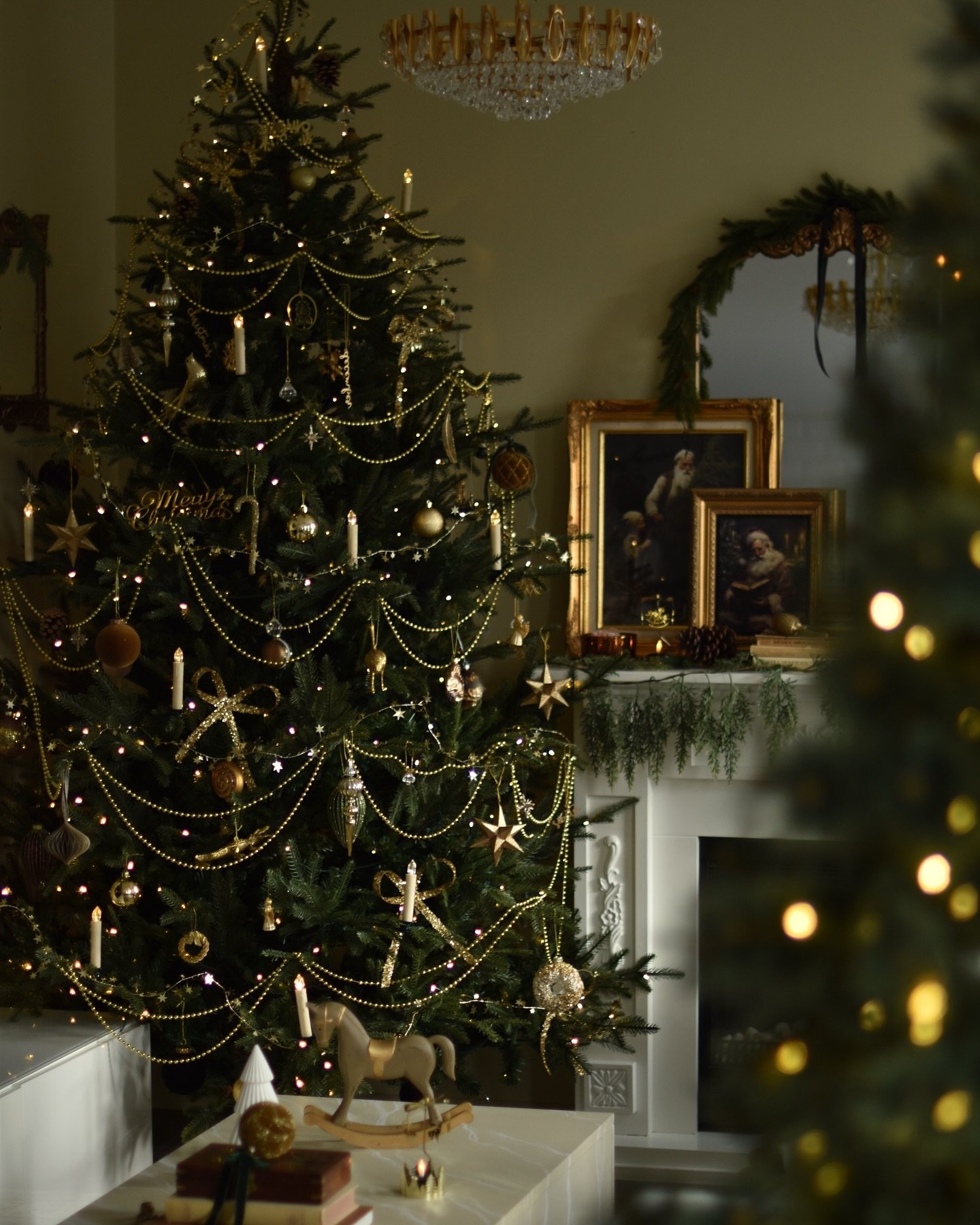 A dark, moody Christmas tree decorated with draped gold beaded garlands, matte gold ornaments, and electric candle lights in a classic European style.