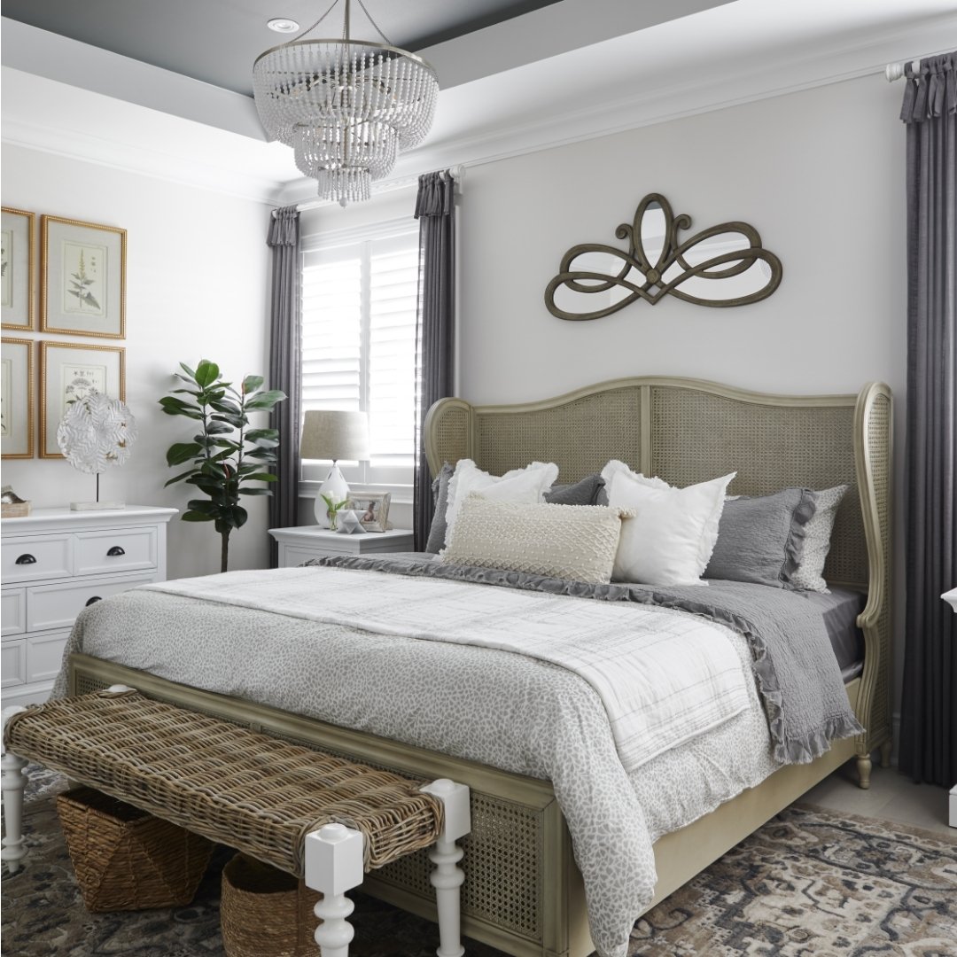 A cozy bedroom with a light gray wicker headboard, white dresser, and a woven bench at the foot of the bed.