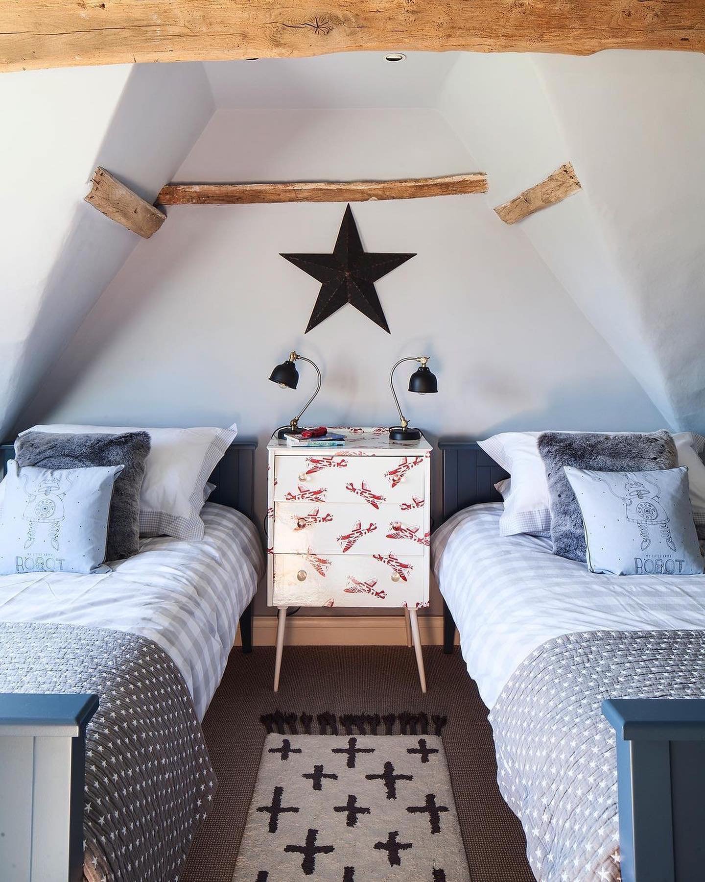 A cozy attic twin bedroom with two beds under a sloped ceiling and an airplane-patterned dresser between them.