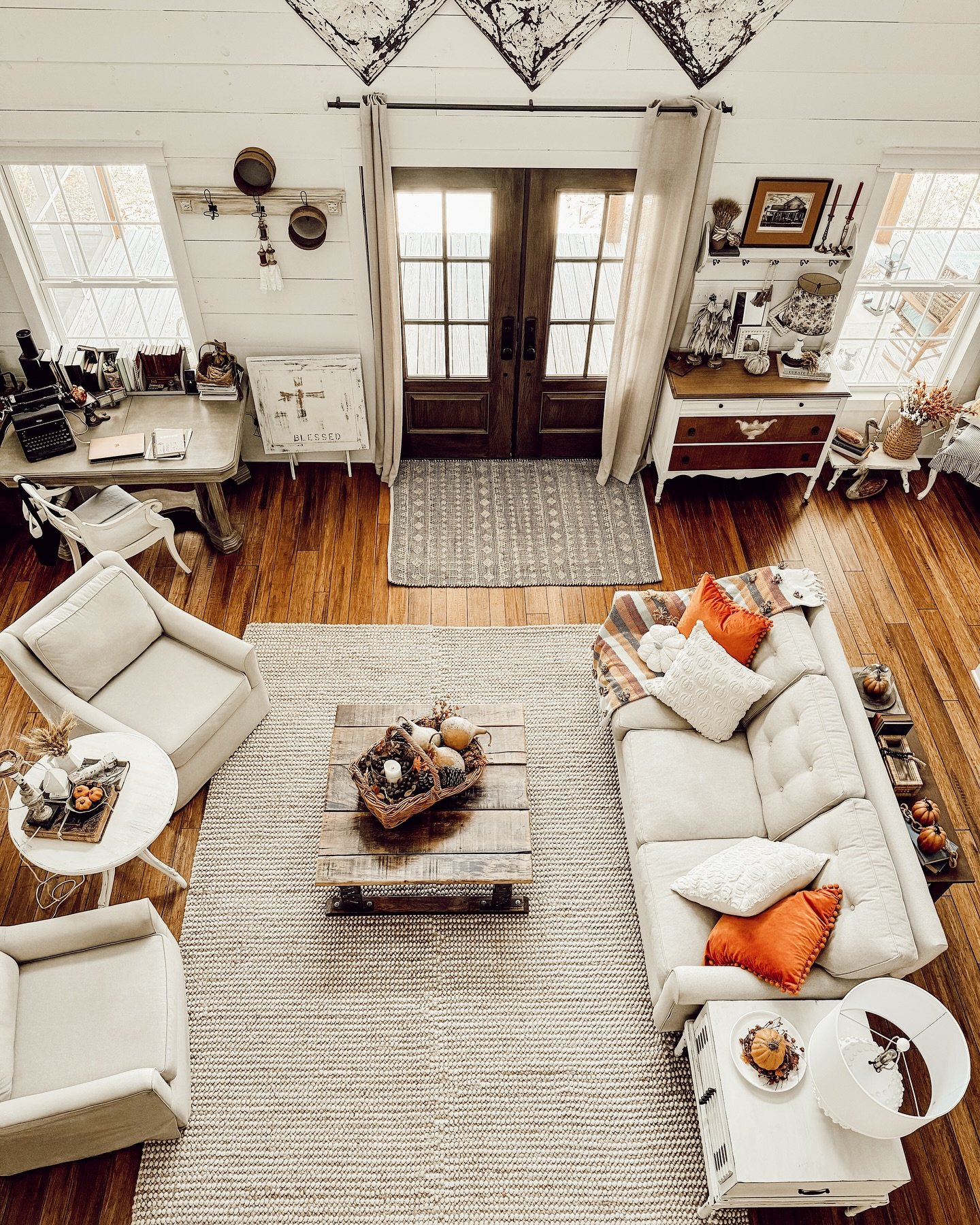 Aerial view of a rustic living room with a neutral-colored sofa, two armchairs, and a wooden coffee table with a basket of pumpkins.