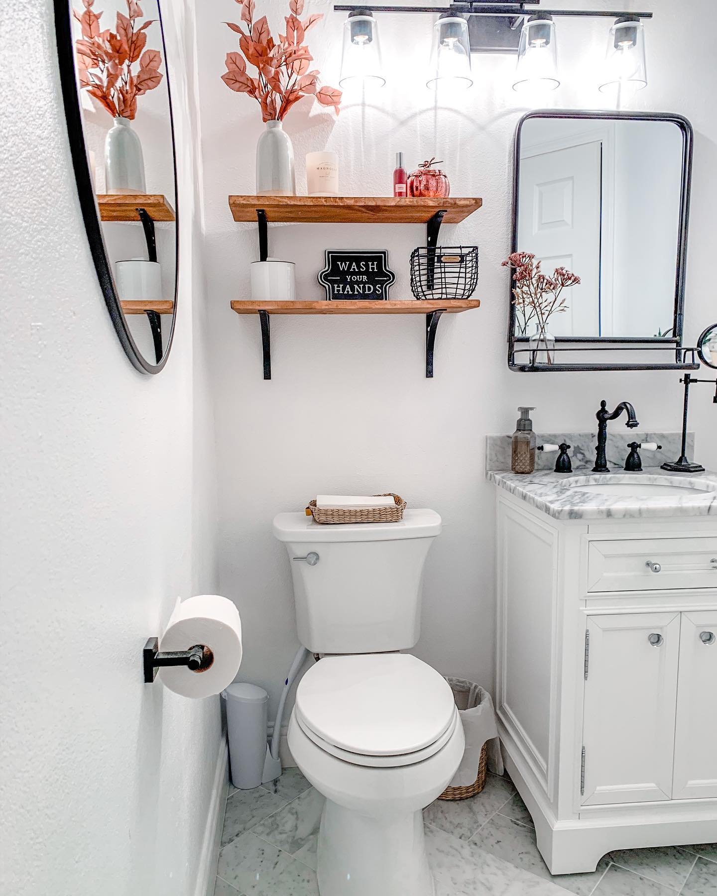 A small, white bathroom with marble floors and black fixtures, decorated with simple fall foliage and a small pink pumpkin.