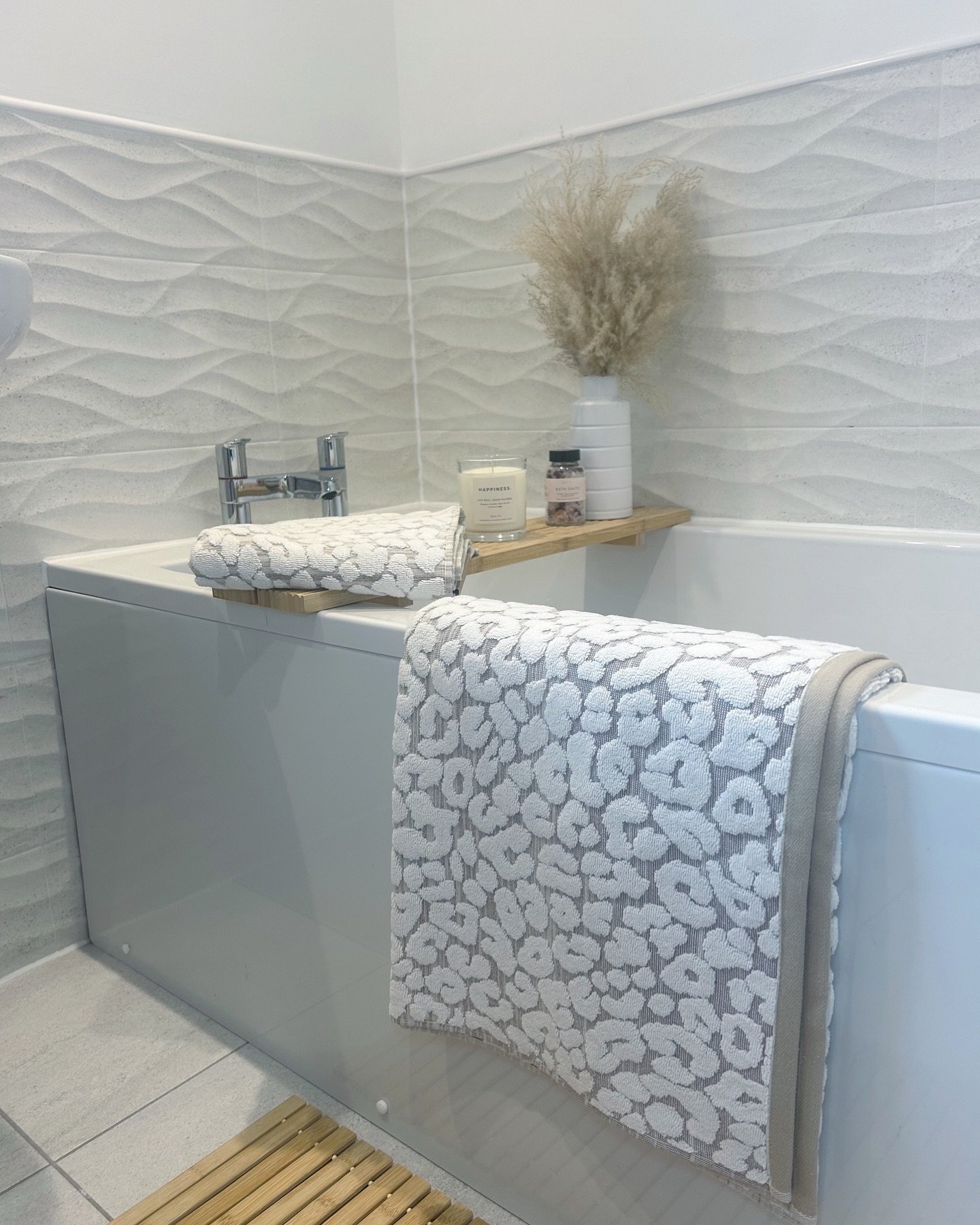 Grey and white leopard print towel draped over a white tub with a small wooden tray holding bath accessories.