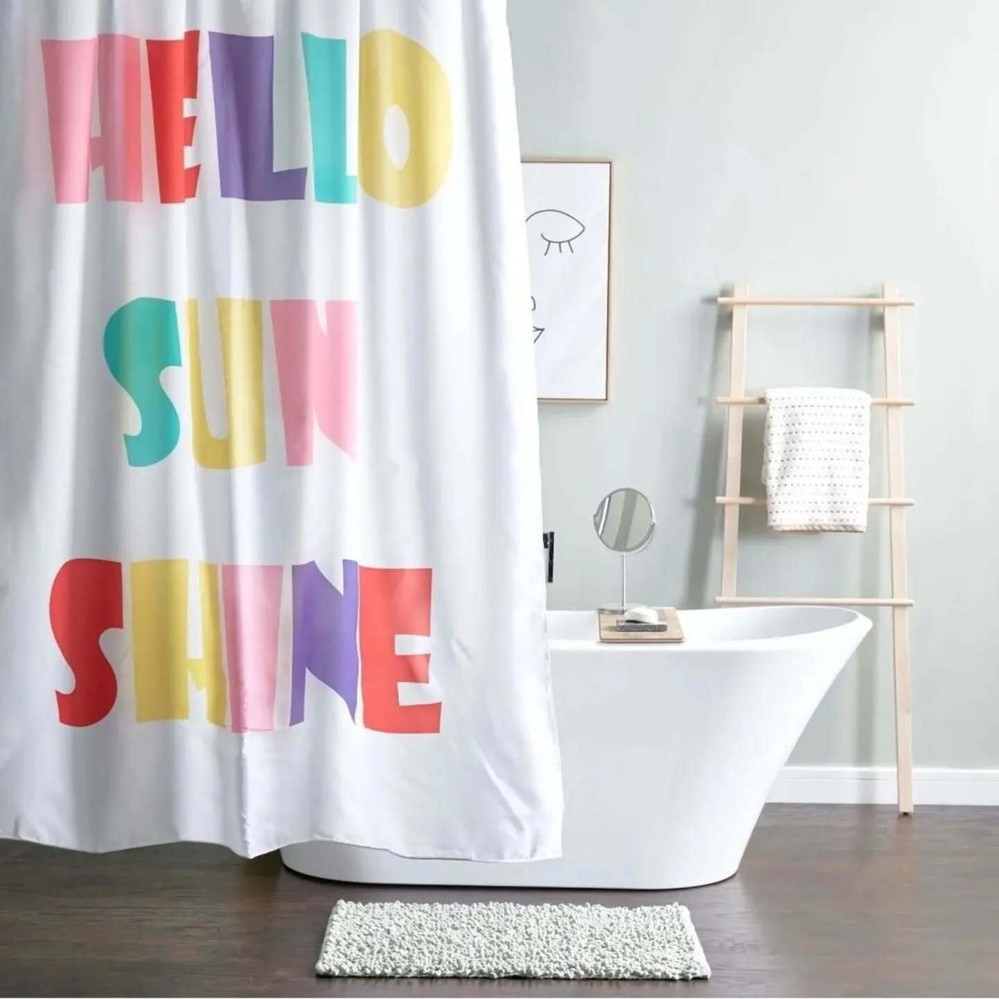 A white shower curtain printed with the words "HELLO SUN SHINE" in large, mixed-font, bright rainbow colors.