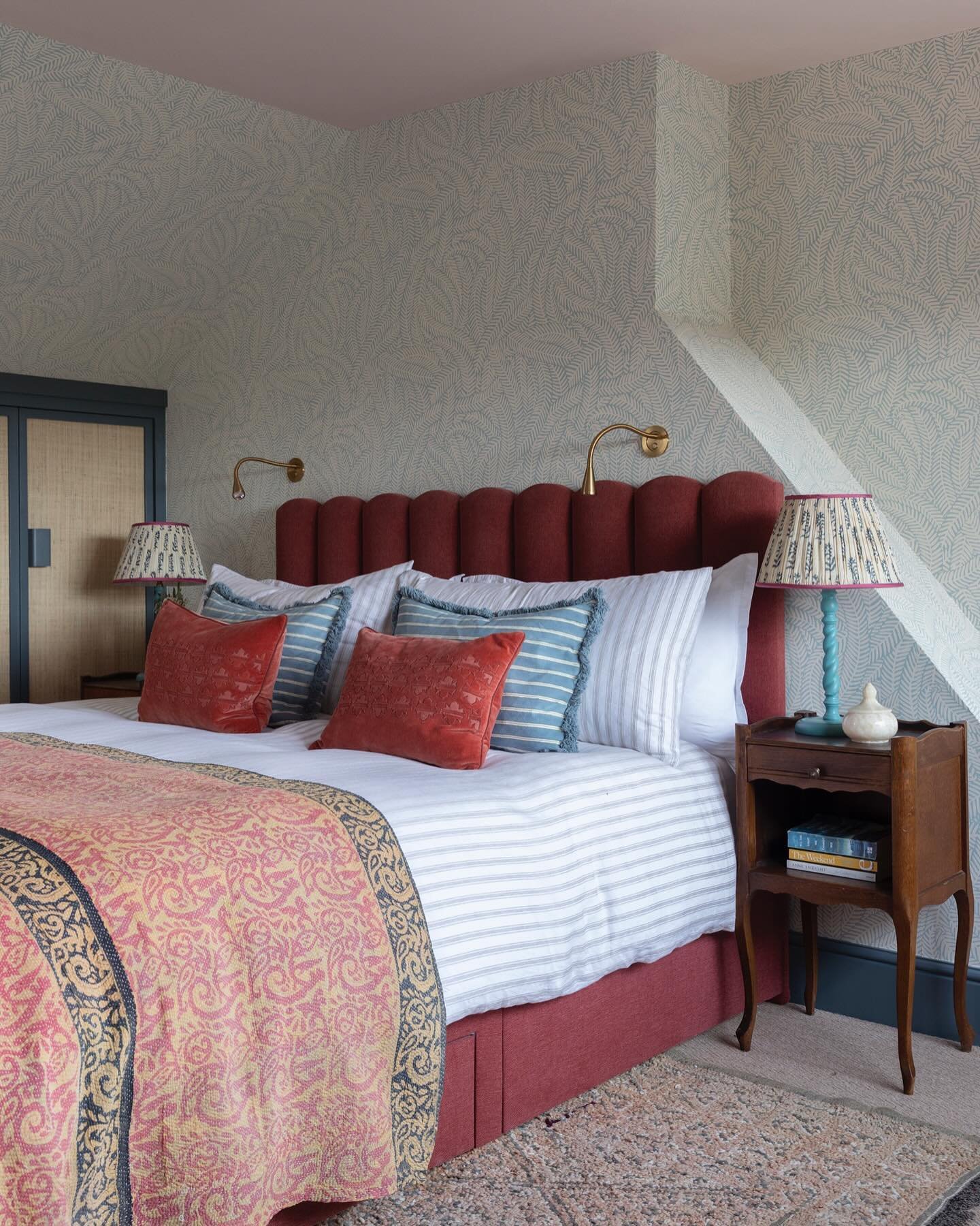 A colorful and eclectic loft bedroom with a blue leaf-patterned wallpaper, a red bed, and a mix of patterned bedding.