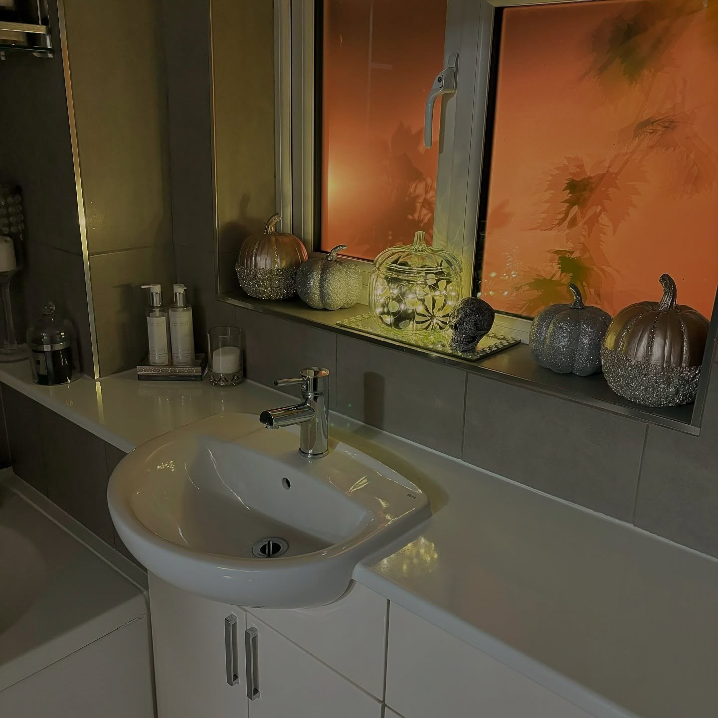 A bathroom with a window decorated with a collection of metallic and glitter-covered pumpkins.