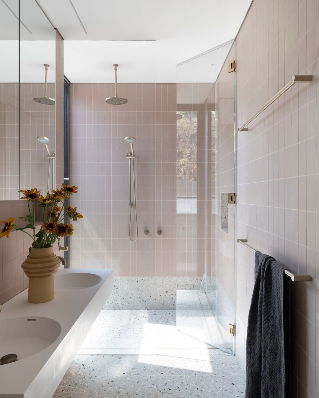 A bright, minimalist bathroom with a two-tone design featuring soft pink subway tiles on the upper walls and speckled gray terrazzo-style tiles on the lower walls and floor.