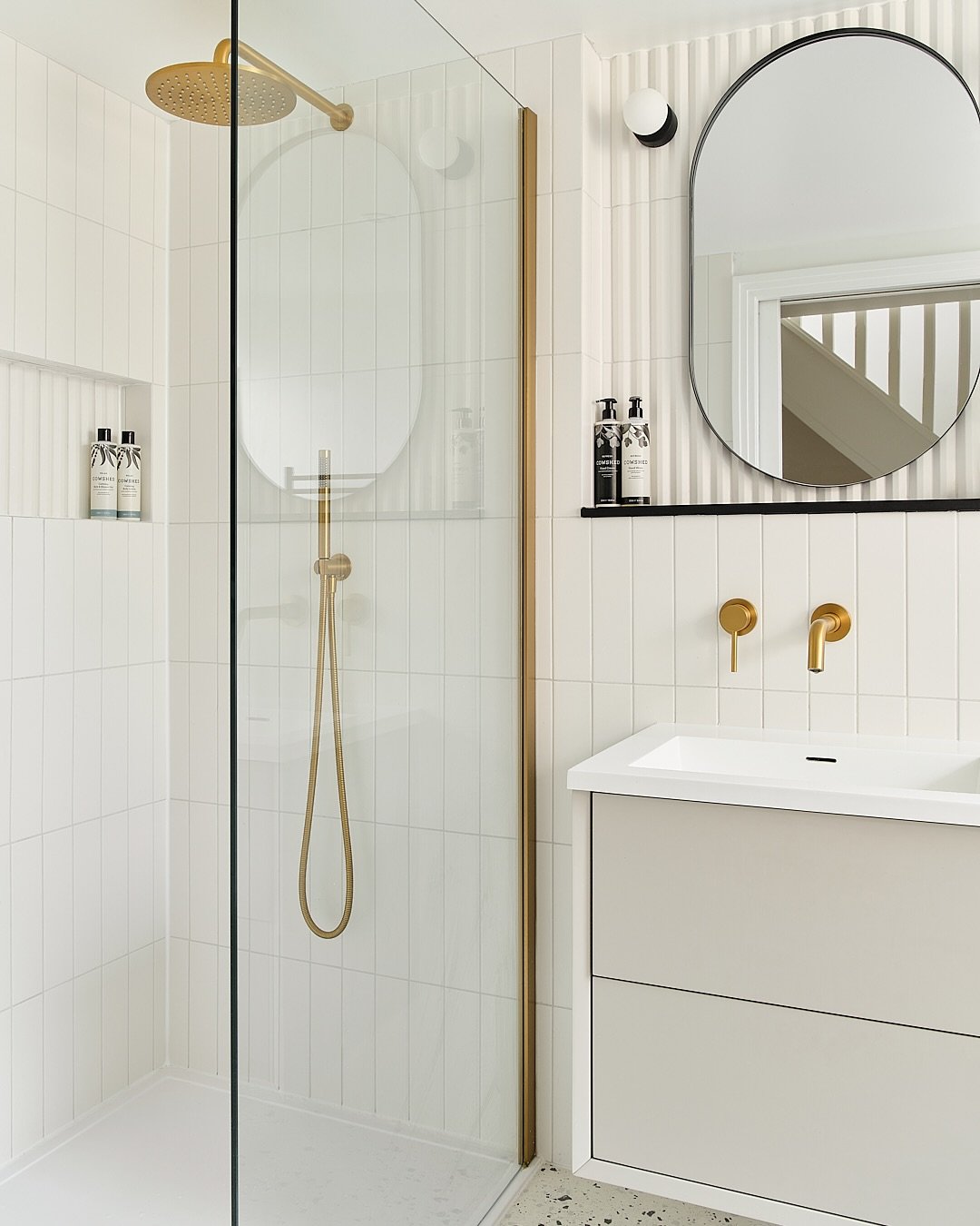 A contemporary walk-in shower featuring vertically stacked white subway tiles, brushed gold fixtures, and a slim gold frame on the glass enclosure.