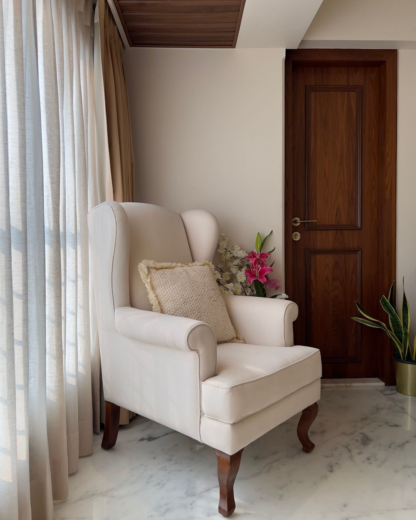A classic white wingback armchair with a textured pillow sits in a bedroom corner on a marble floor.